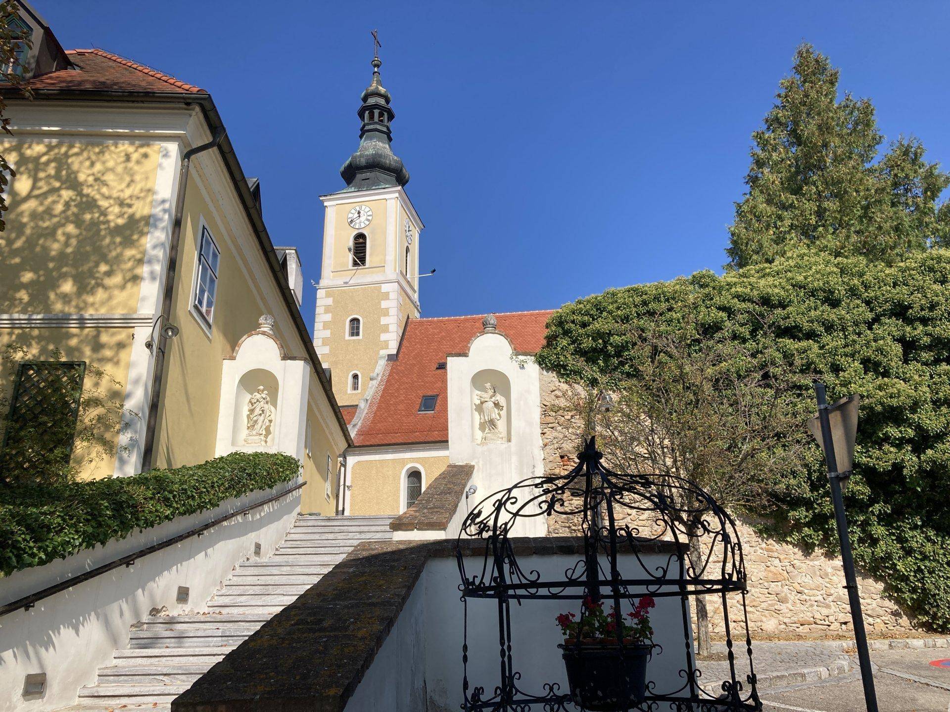 Historische Kirche mit Glockenturm und umliegenden Gebäuden unter blauem Himmel.