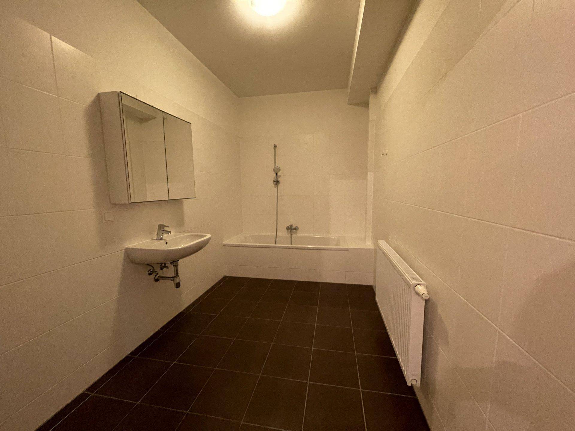 Badezimmer mit Badewanne, Waschbecken, Spiegelschrank und weißen Wandfliesen.
