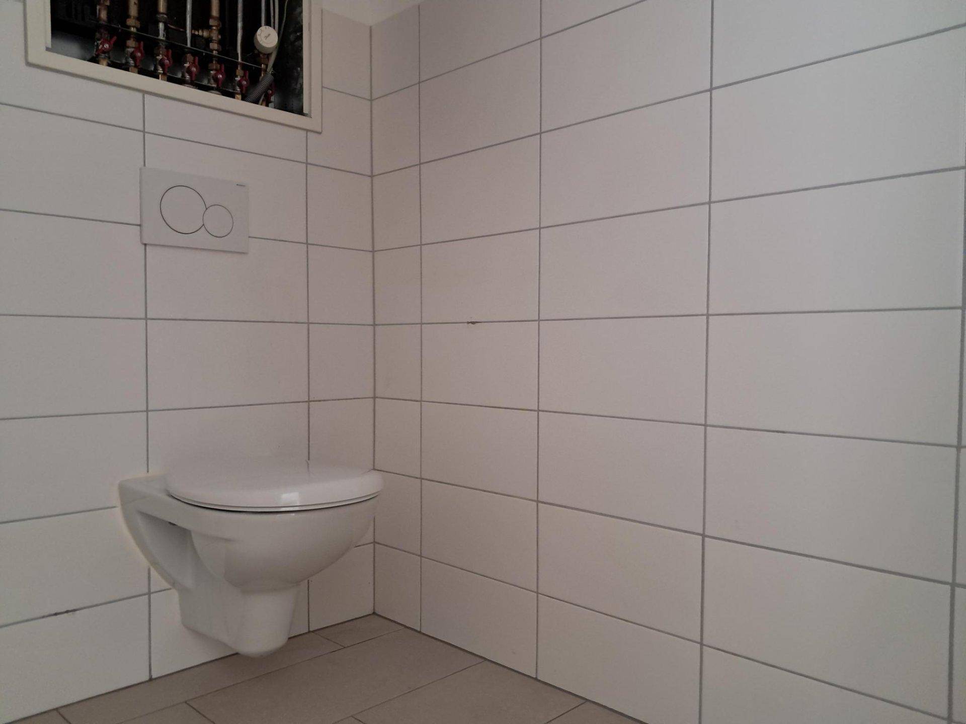 Sauberer Toilettenbereich mit wandhängendem WC und weißen Fliesen an den Wänden.