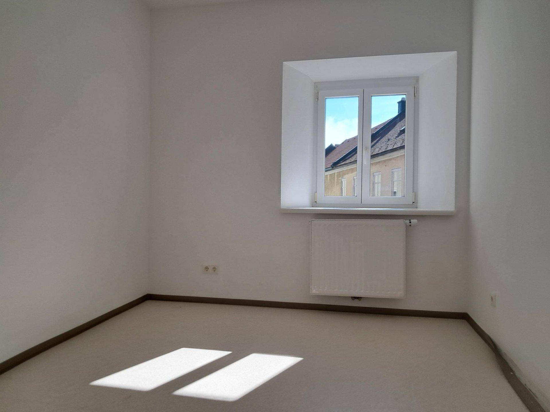 Helles Schlafzimmer mit einem Fenster, das viel Tageslicht hereinlässt und einen Ausblick bietet.