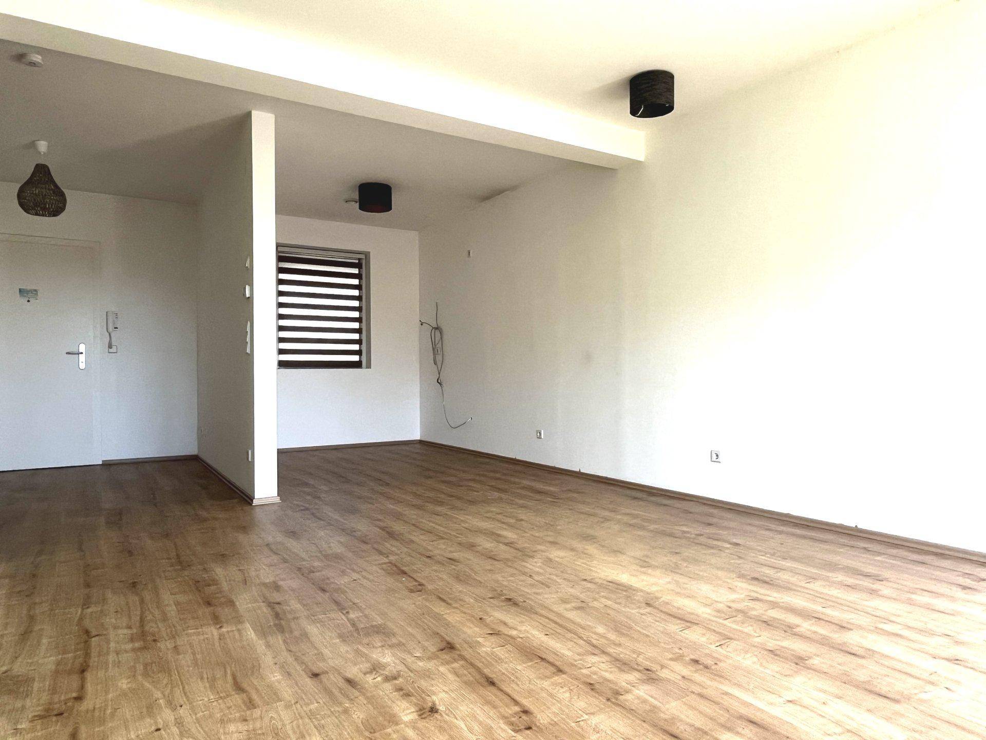 Offener Wohnbereich mit Laminatboden und einem Fenster mit Jalousien, bereit zur individuellen Gestaltung.