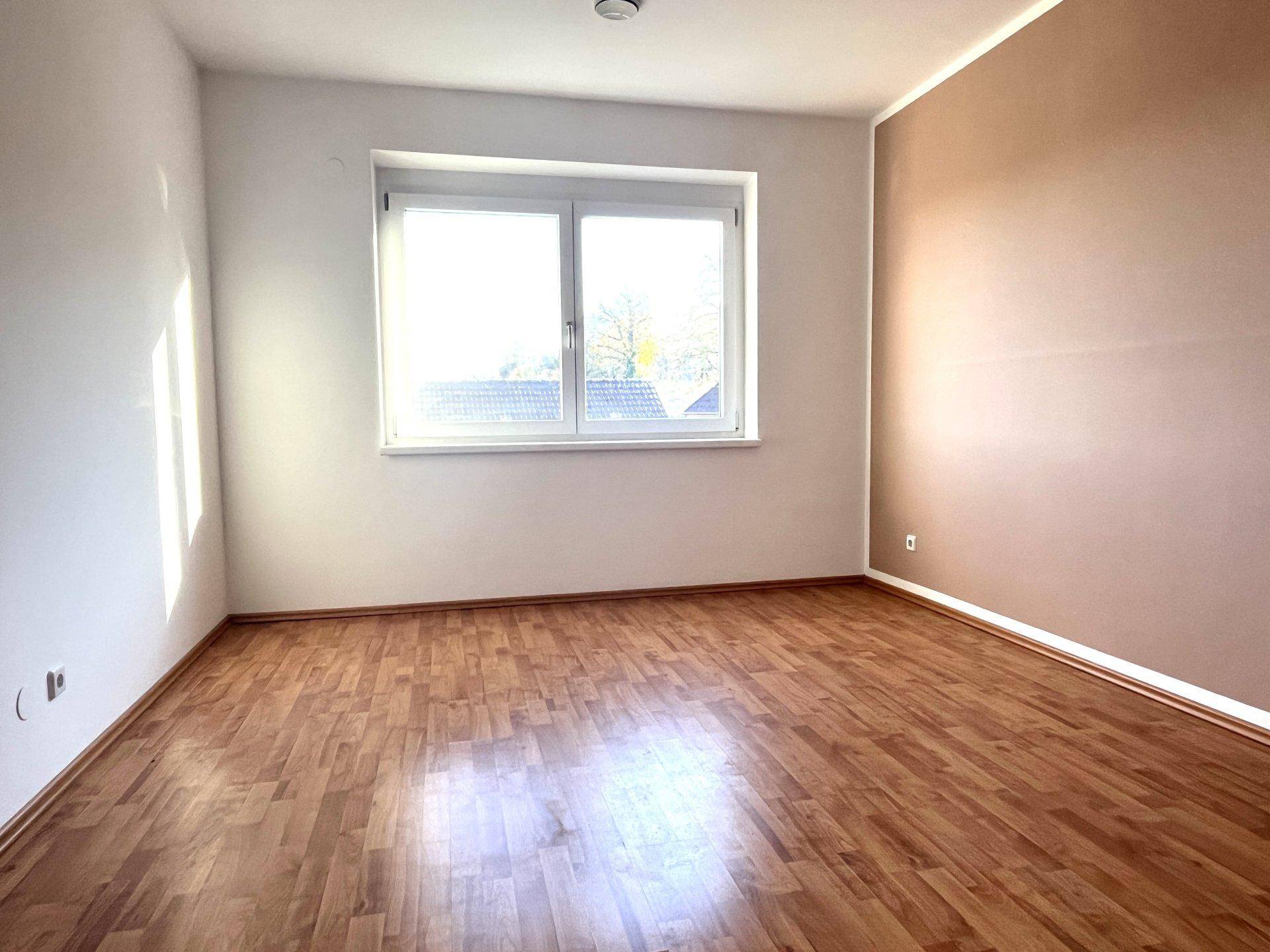 Helles Schlafzimmer mit Laminatboden und einem großen Fenster, das viel natürliches Licht bietet.