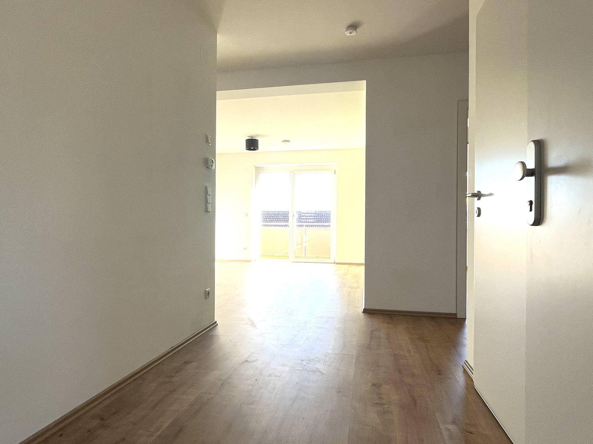 Heller Flur mit Laminatboden, der zu einem lichtdurchfluteten Wohnbereich mit Balkonzugang führt.