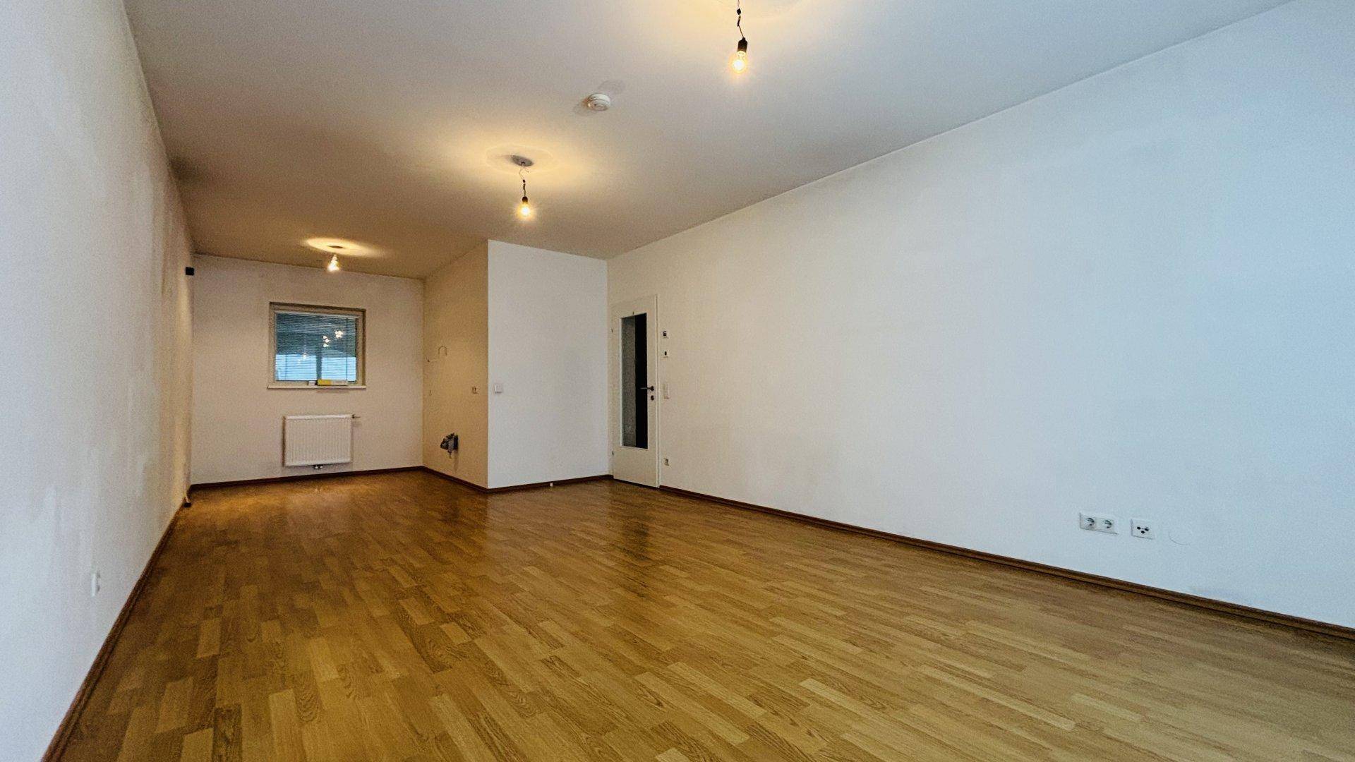 Geräumiges, leeres Wohnzimmer mit hellem Parkettboden und weißen Wänden, bereit zur Einrichtung.