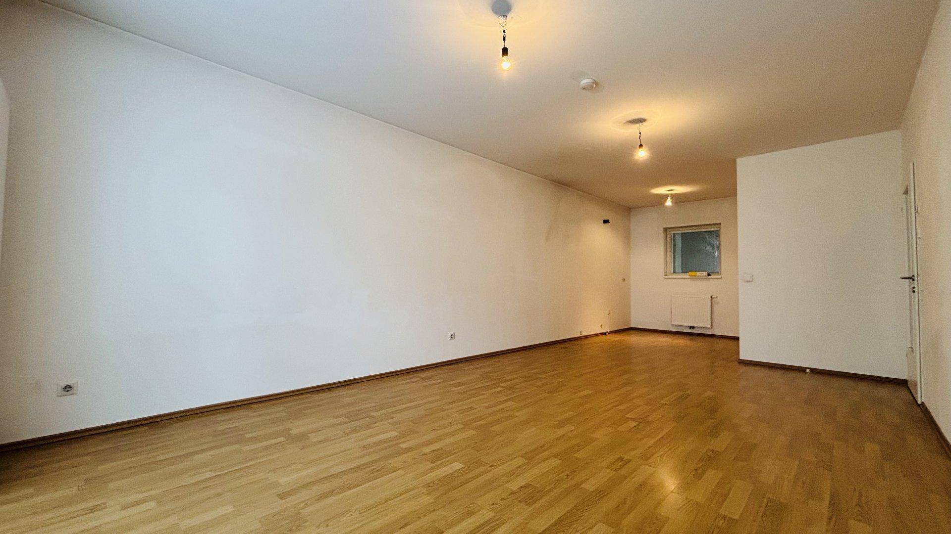 Helles, leeres Wohnzimmer mit Parkettboden und weißen Wänden, ideal für individuelle Gestaltung.