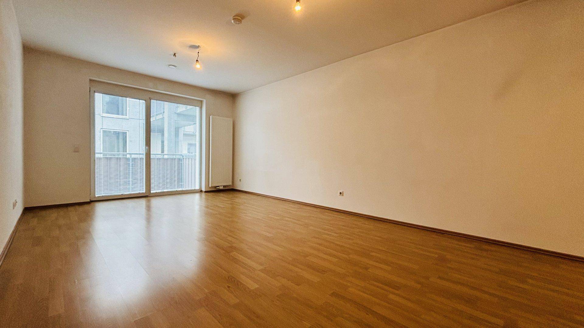 Heller Wohnbereich mit Parkettboden und Zugang zu einem französischen Balkon, der viel Licht hereinlässt.