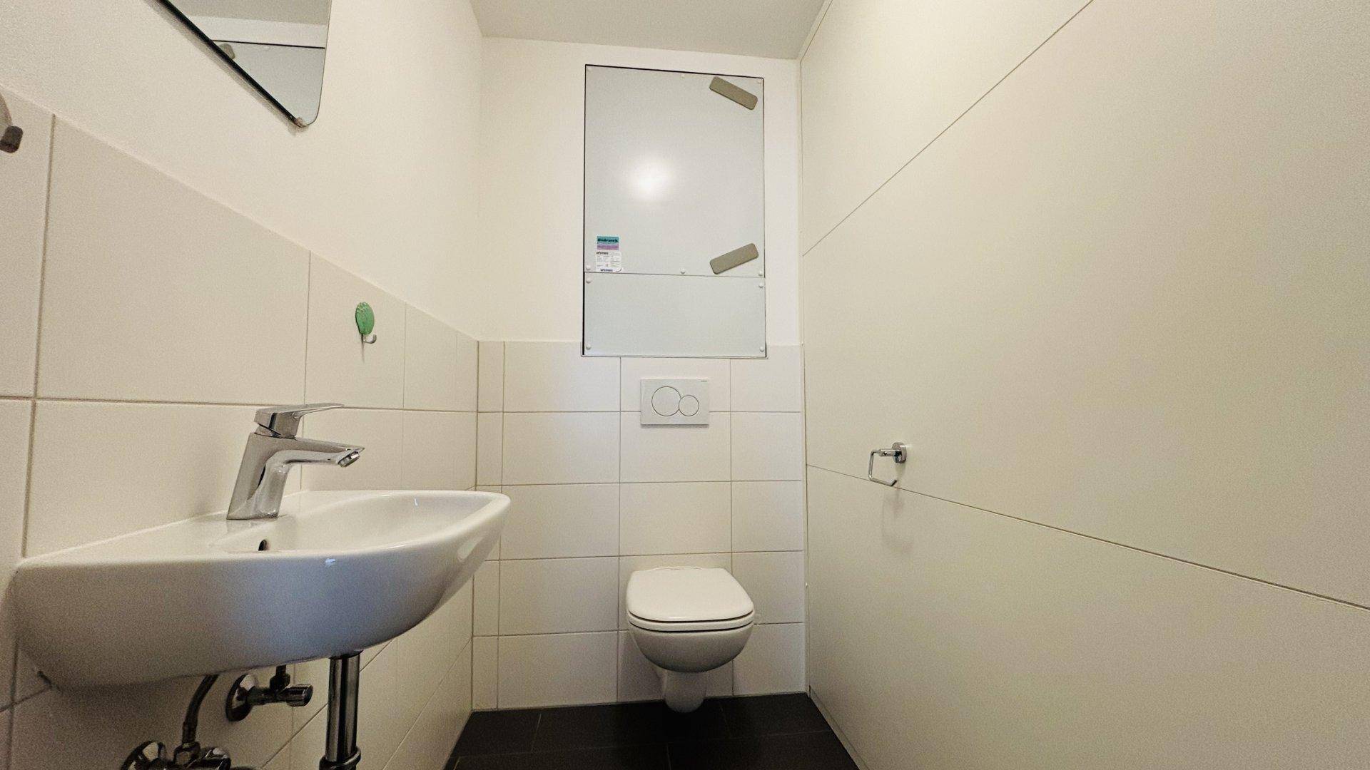 Separates WC mit wandhängender Toilette, Waschbecken und weißen Fliesen, funktional und sauber.