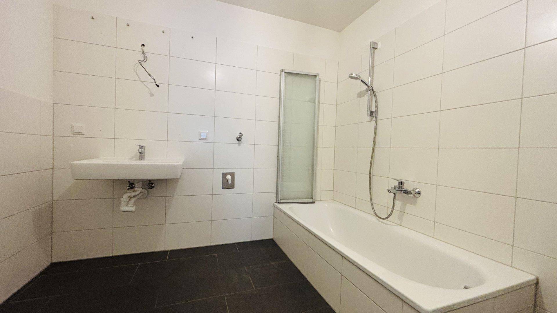 Modernes Badezimmer mit weißen Fliesen, Badewanne und Waschbecken, bereit zur Nutzung.
