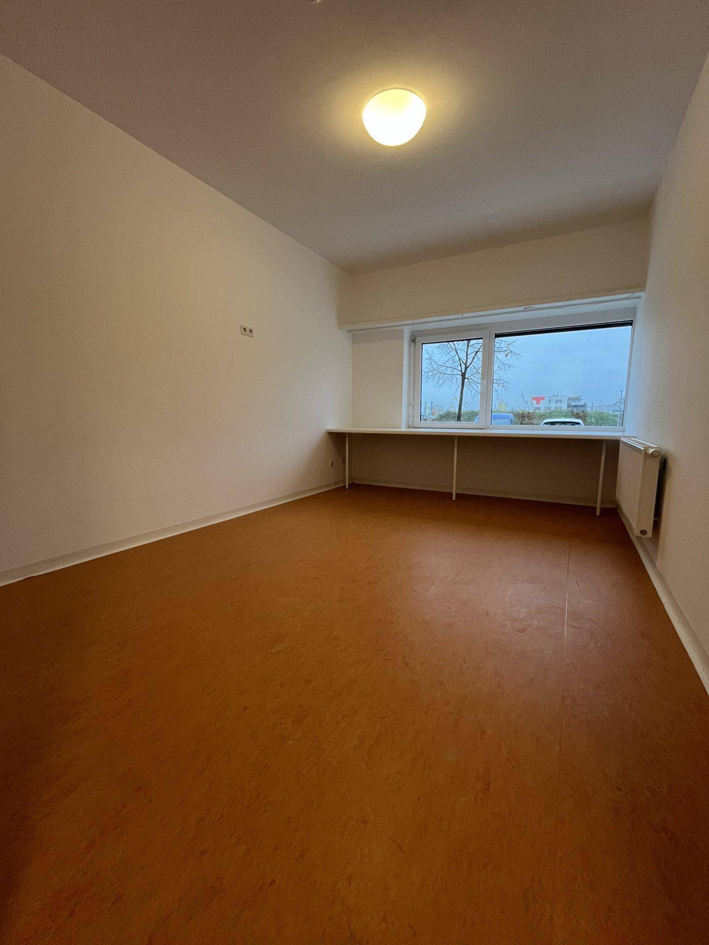 Leeres Zimmer mit breitem Fenster und Heizkörper, bereit zur individuellen Einrichtung.