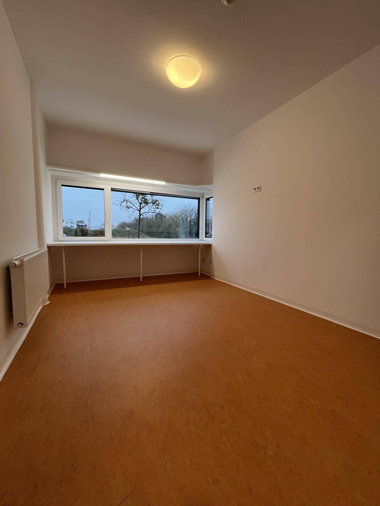 Helles Schlafzimmer mit großem Fenster und einem langen Regal unter der Fensterbank.