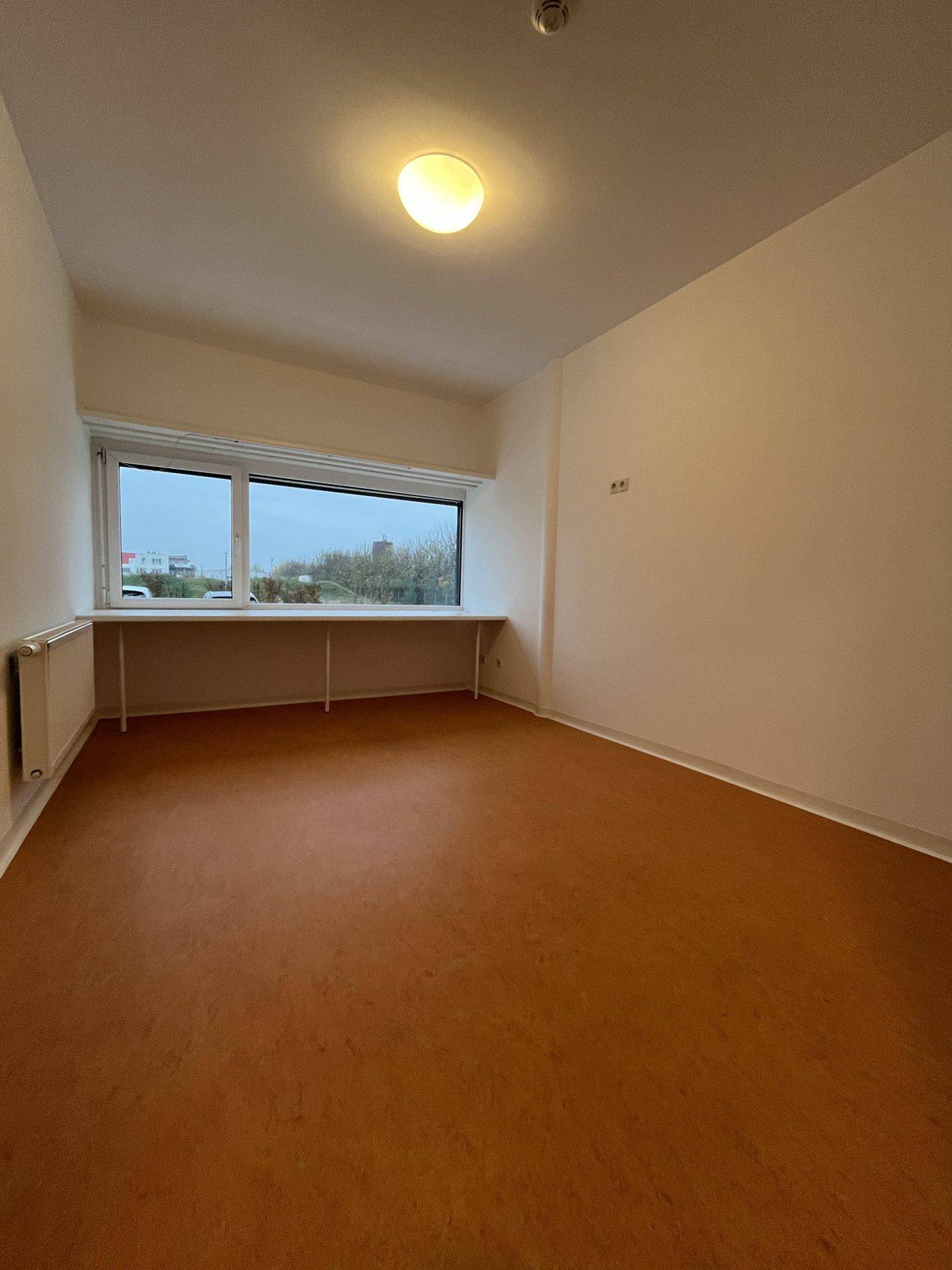 Geräumiges Zimmer mit viel Tageslicht durch ein großes Fenster und einfacher Ausstattung.