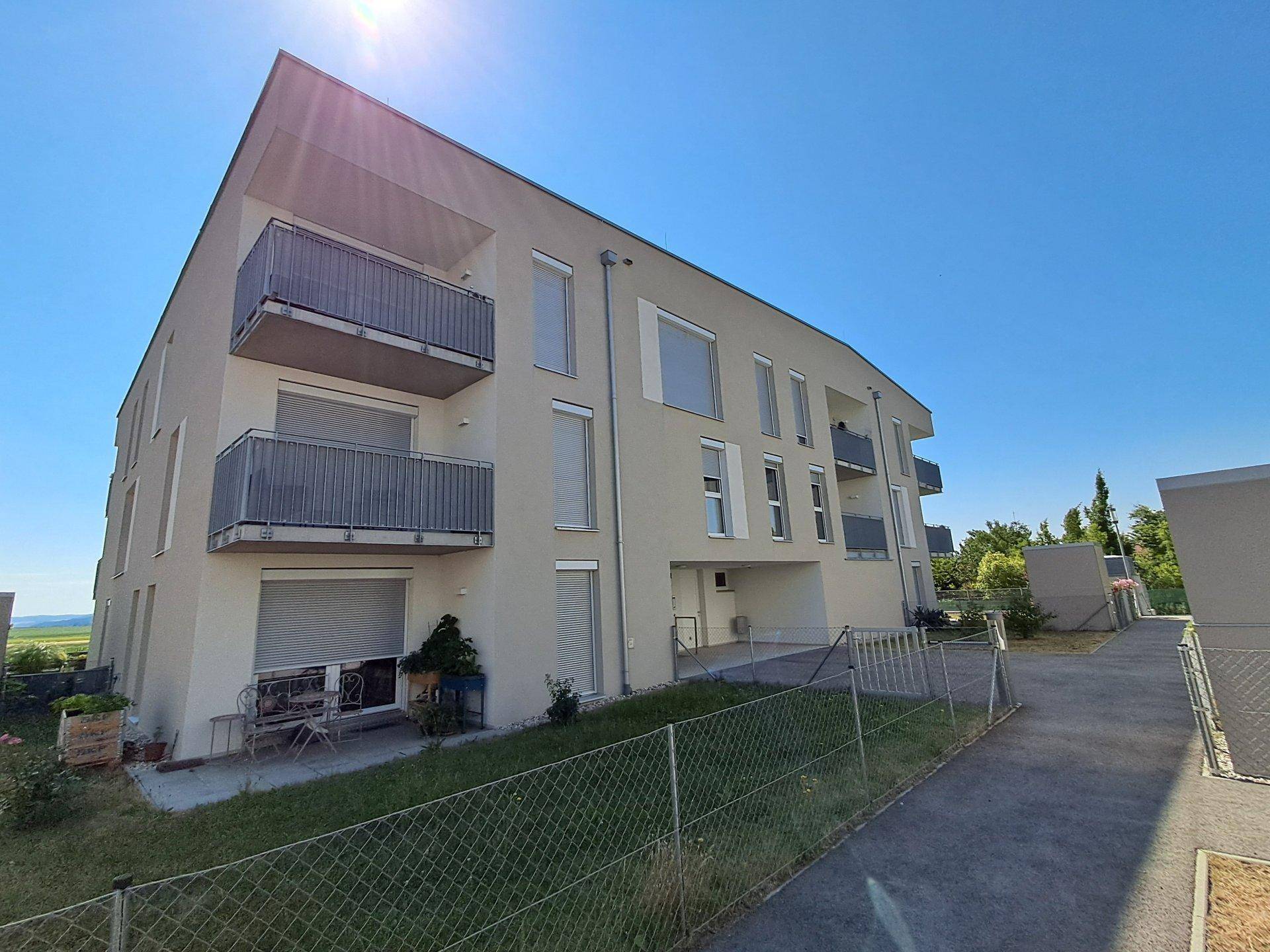 Ansicht des modernen Wohngebäudes mit mehreren Balkonen und einer möblierten Terrasse im Erdgeschoss.