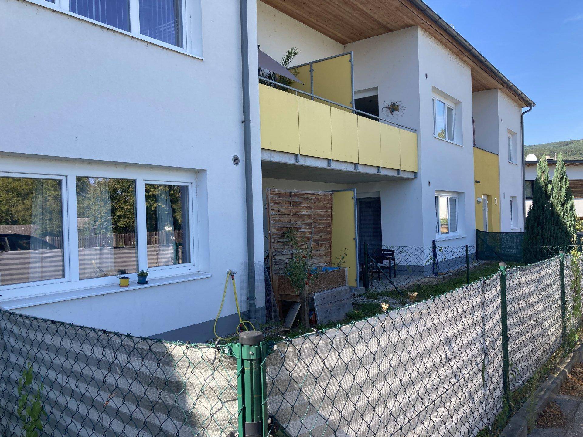 Kleiner privater Gartenbereich im Erdgeschoss mit Balkon darüber und Sichtschutz aus Holz.