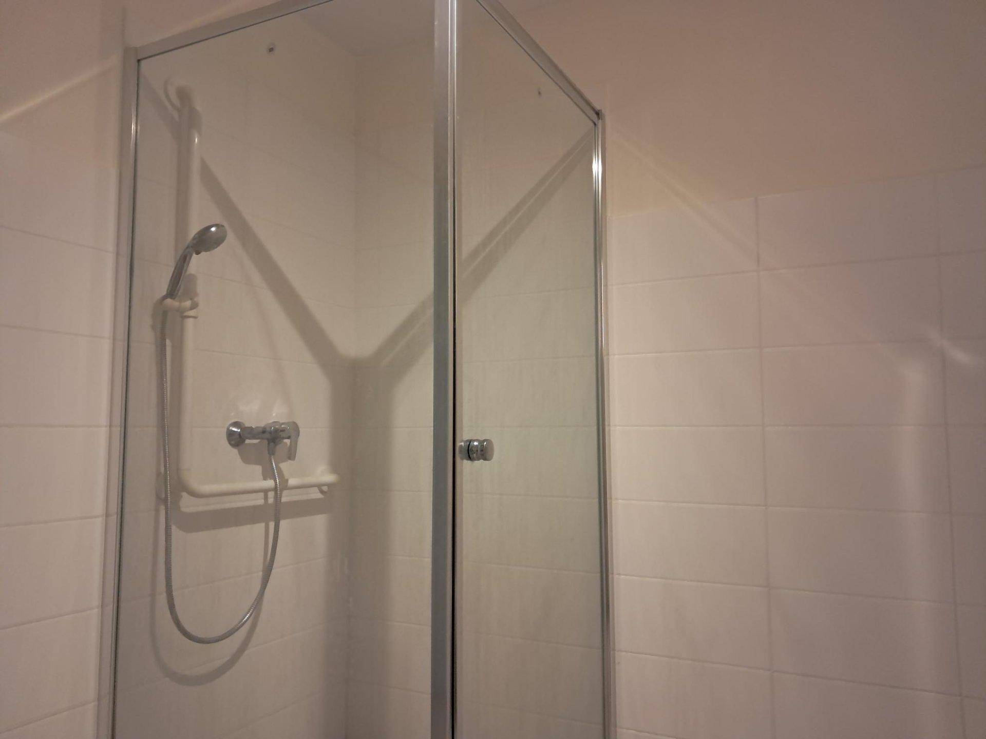 Duschbereich mit Glasabtrennung und Handbrause in einem hell gefliesten Badezimmer.