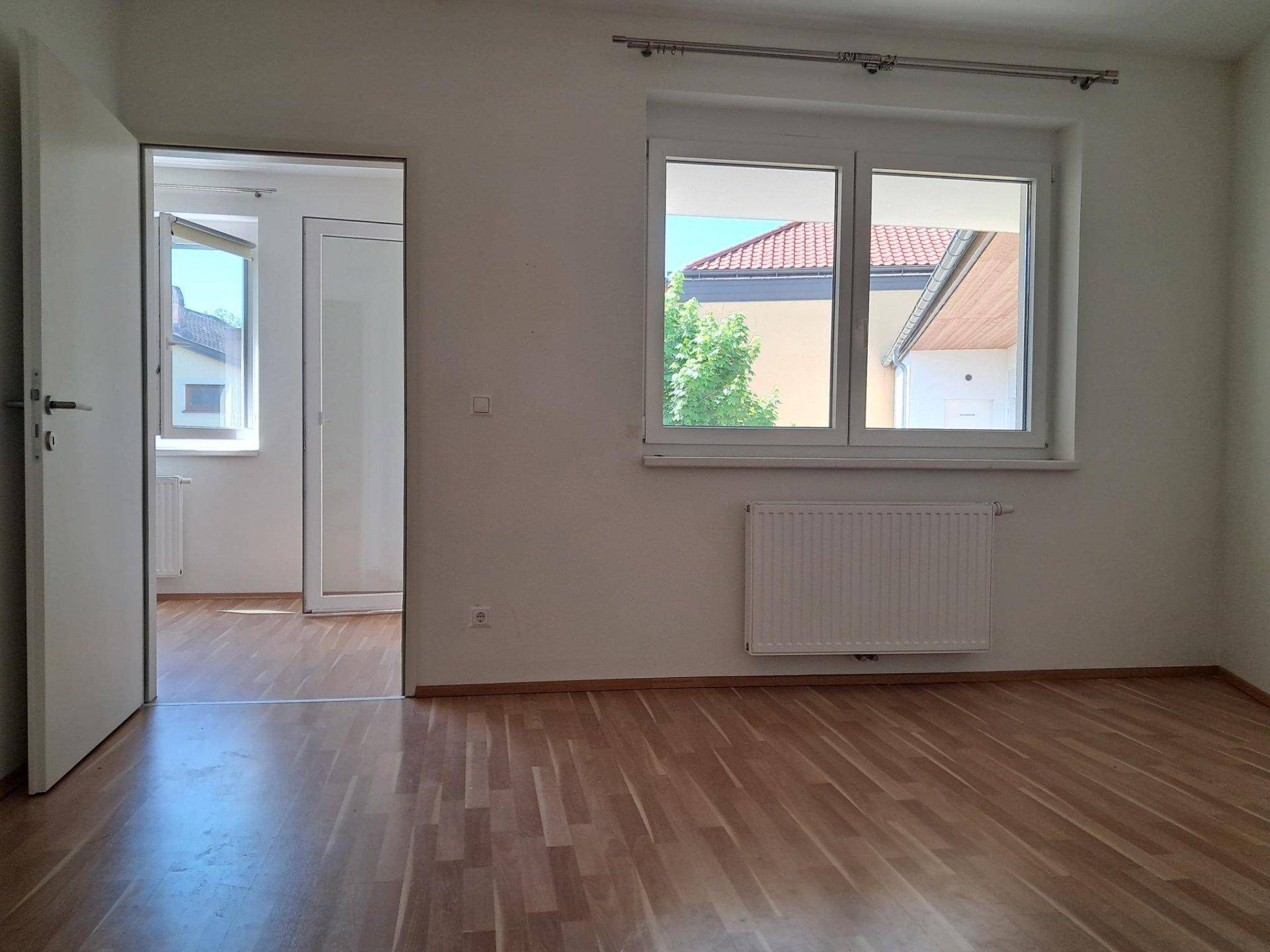 Helles Zimmer mit Laminatboden und Zugang zu einem weiteren Raum, ideal als Schlafzimmer.
