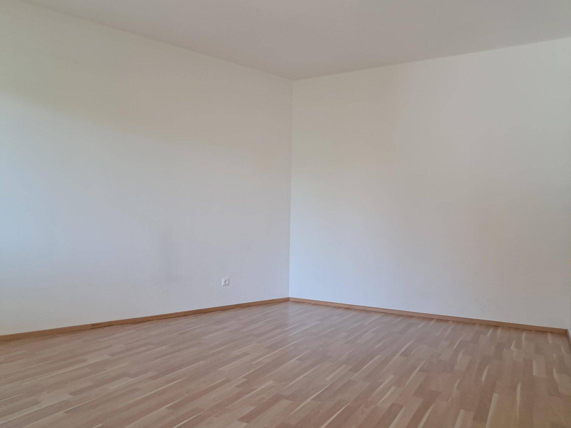Leeres, helles Zimmer mit Laminatboden und weißen Wänden, bereit zur individuellen Gestaltung.