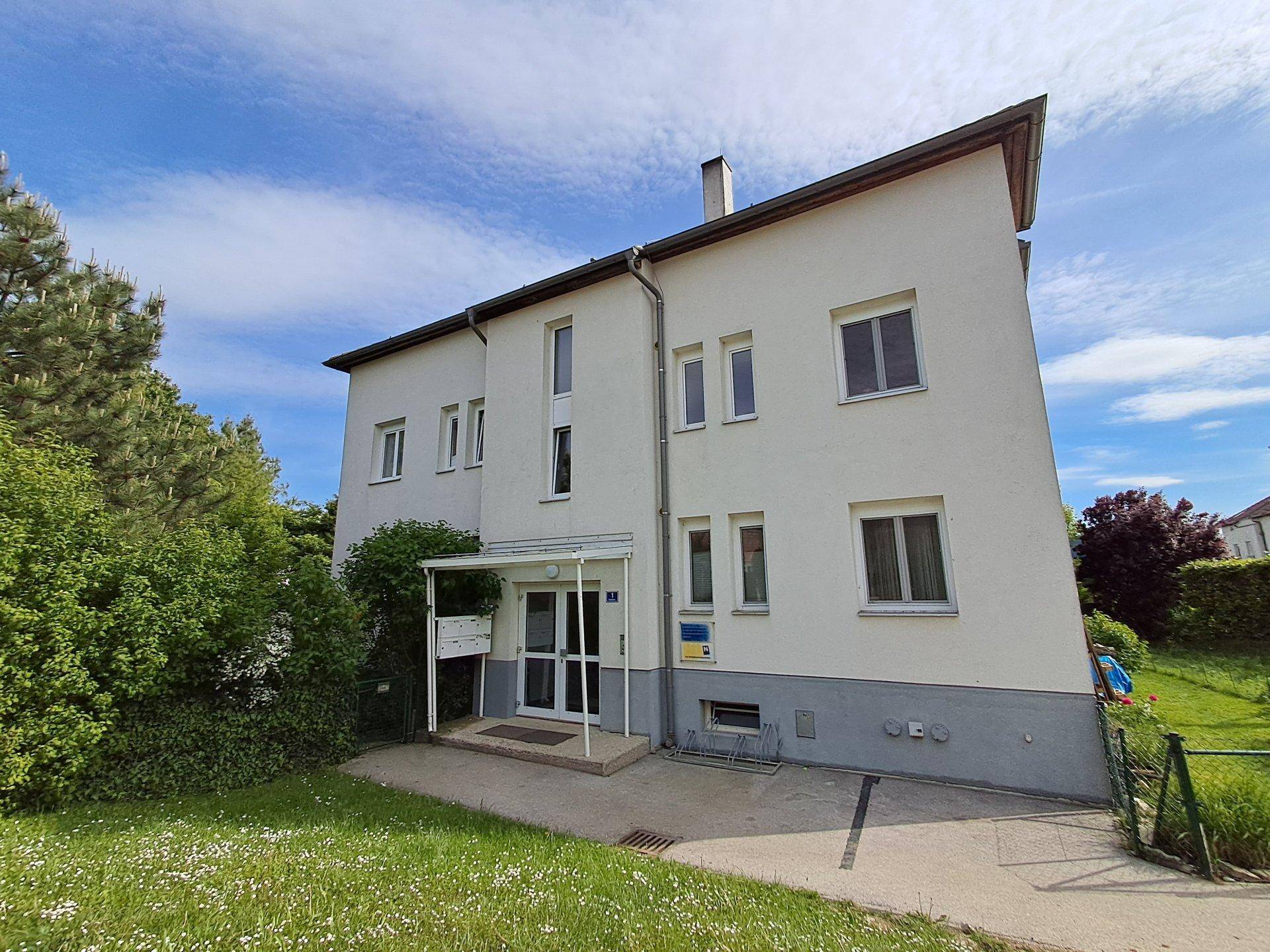 Vorderansicht eines gepflegten Mehrfamilienhauses mit Eingangsbereich und Grünflächen.