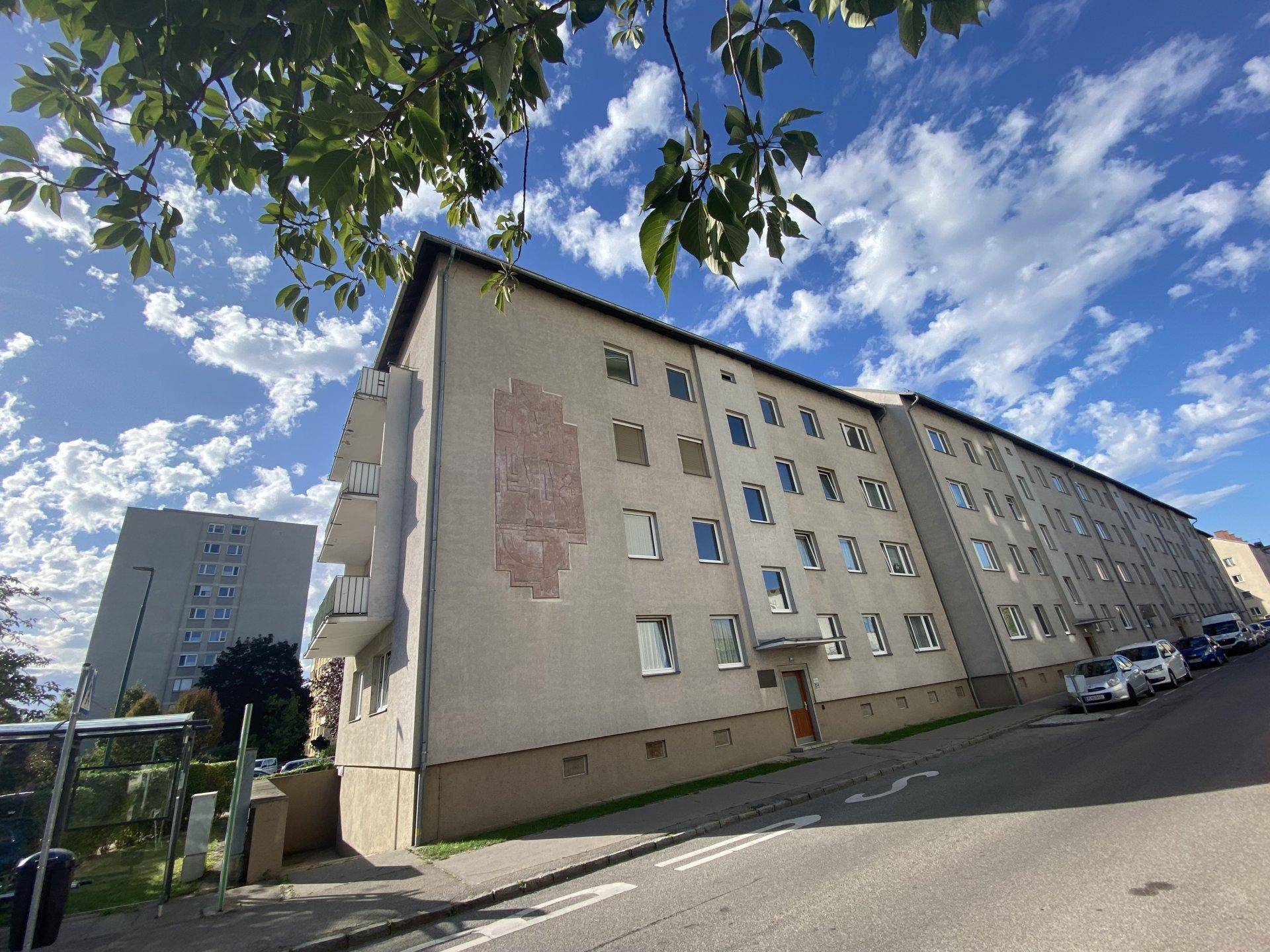 Ansicht der langen Wohngebäudefront entlang der Straße mit Balkonen und geparkten Fahrzeugen.