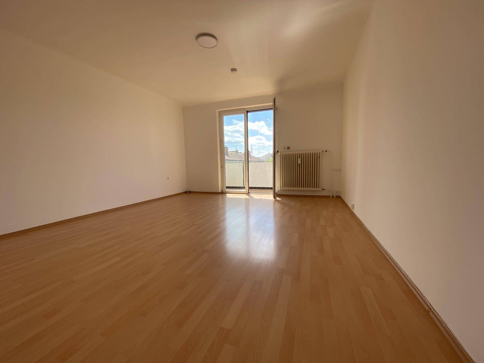 Heller Wohnraum mit Laminatboden und Zugang zu einem Balkon, der viel Tageslicht hereinlässt.