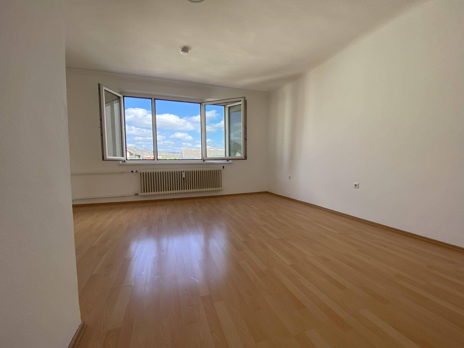 Helles, leeres Zimmer mit Laminatboden und einem breiten Fensterbereich, der einen weiten Ausblick bietet.