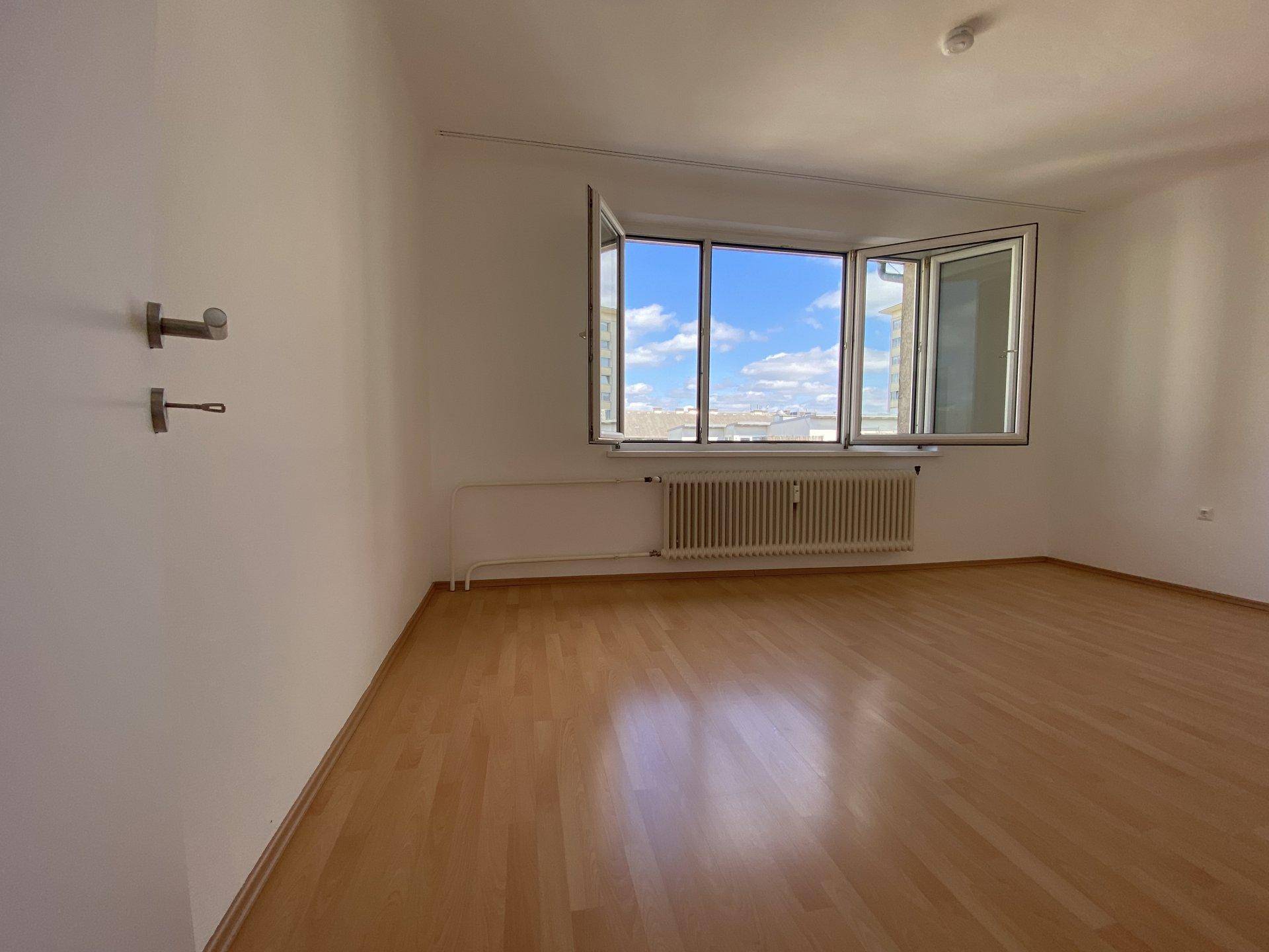 Geräumiges, leeres Zimmer mit hellem Laminatboden und einem großen Erkerfenster, das viel Licht hereinlässt.