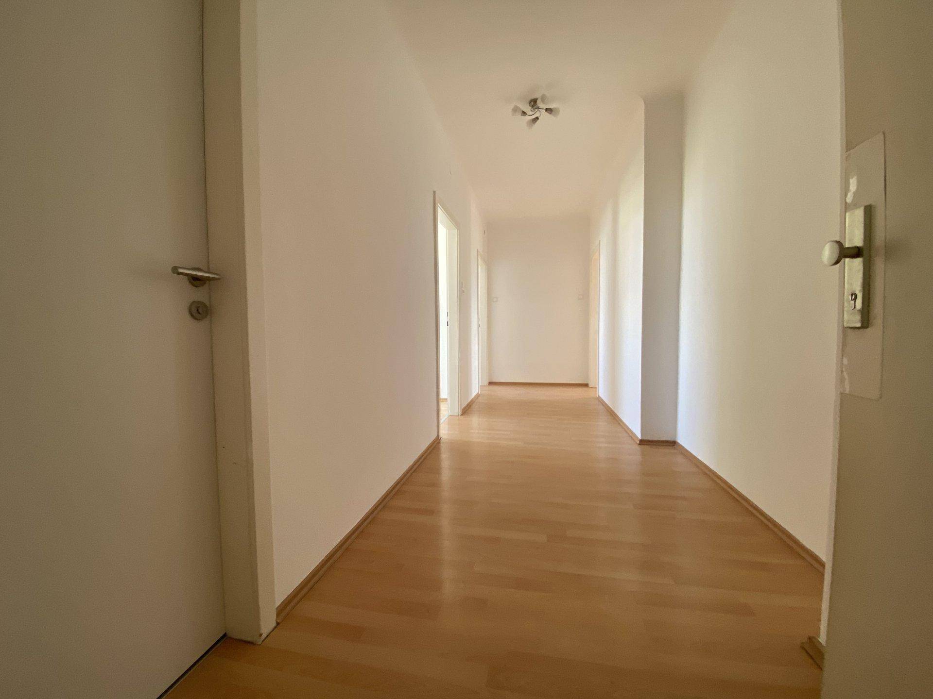 Heller Flur mit hellem Laminatboden und weißen Wänden, der zu weiteren Räumen führt.