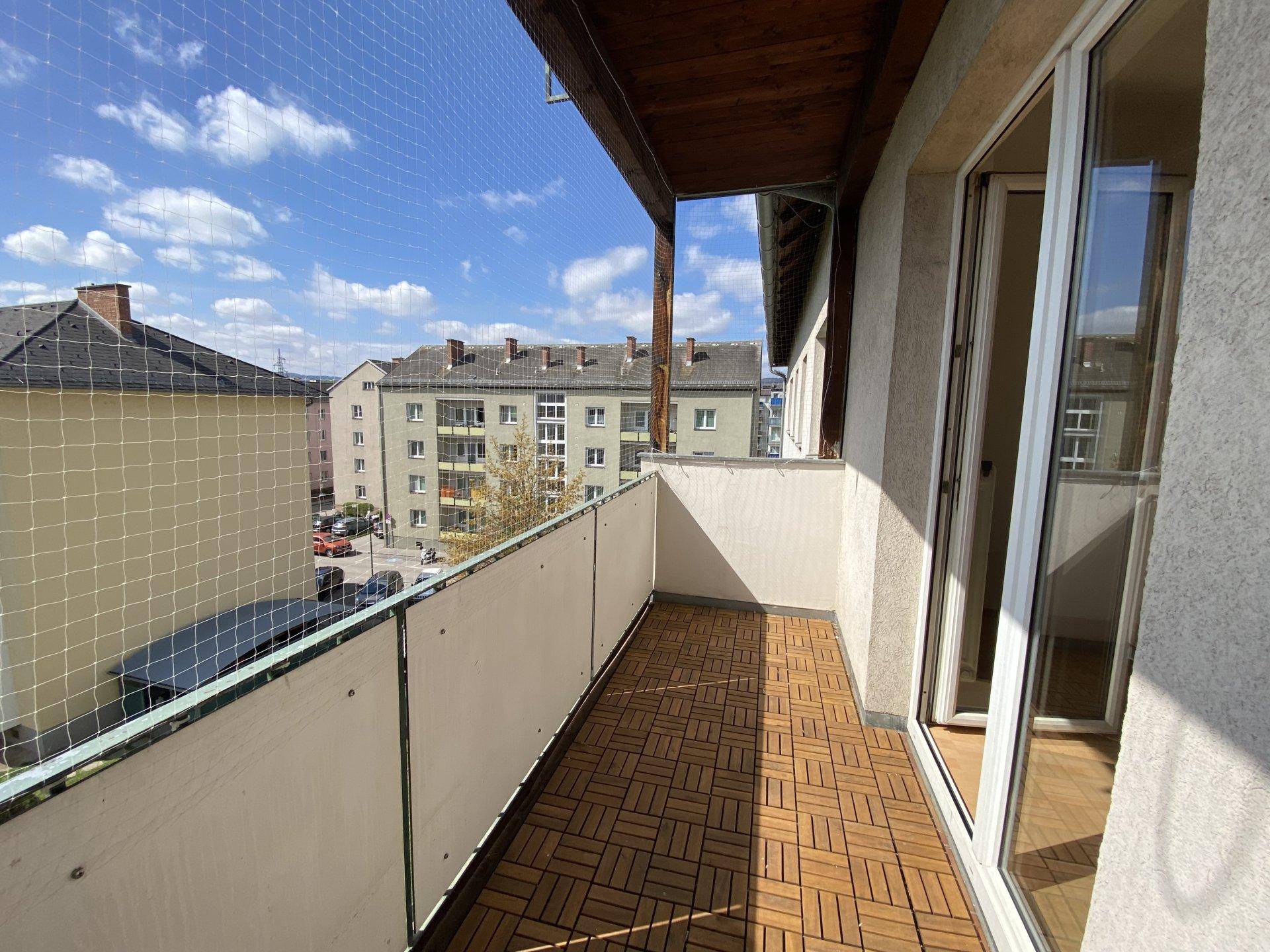 Geräumiger Balkon mit Holzboden und Blick auf die umliegenden Gebäude und den Himmel.