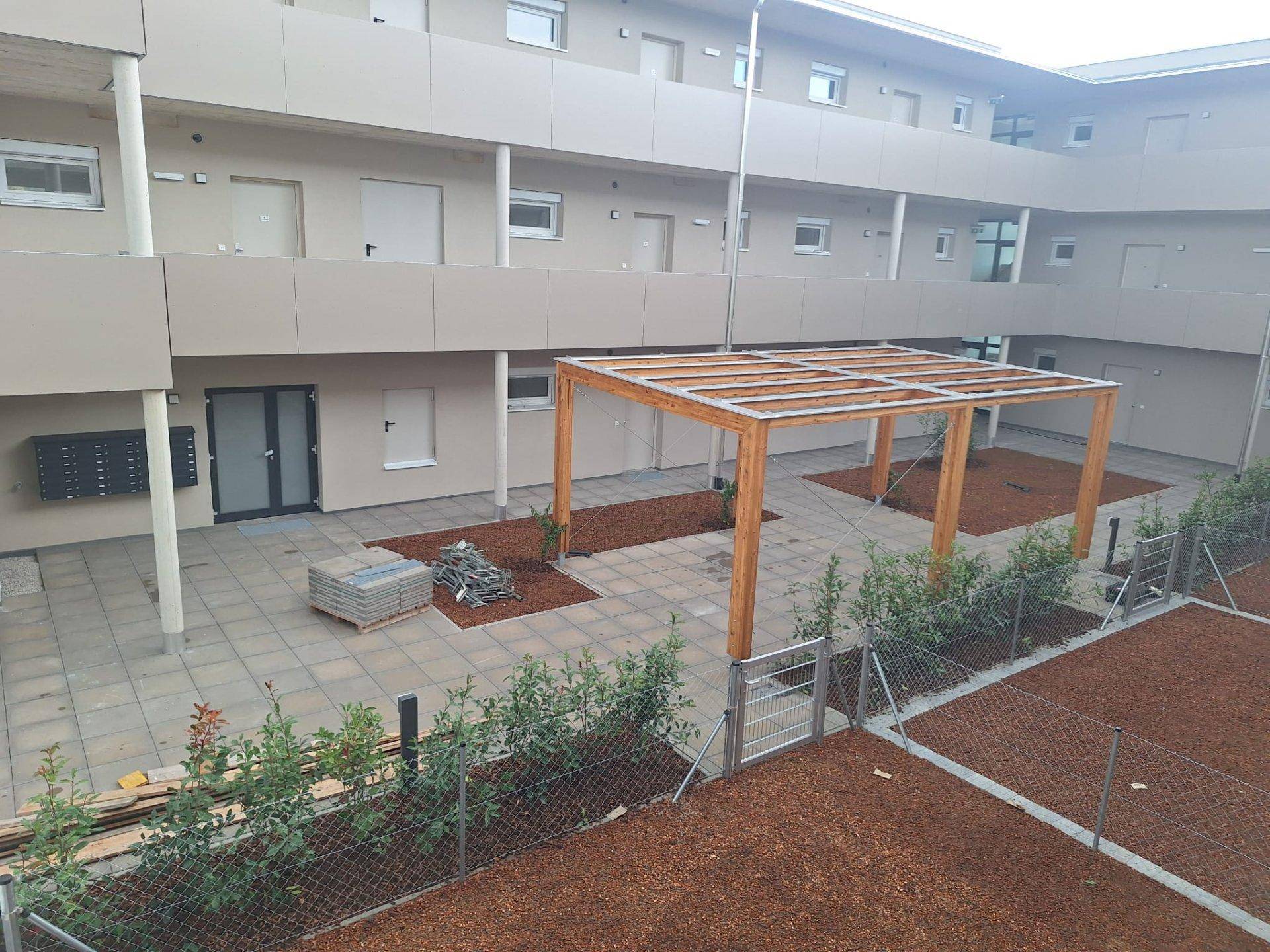 Blick auf den Innenhof eines Wohnkomplexes mit Holzpergola und neu angelegten Grünflächen.