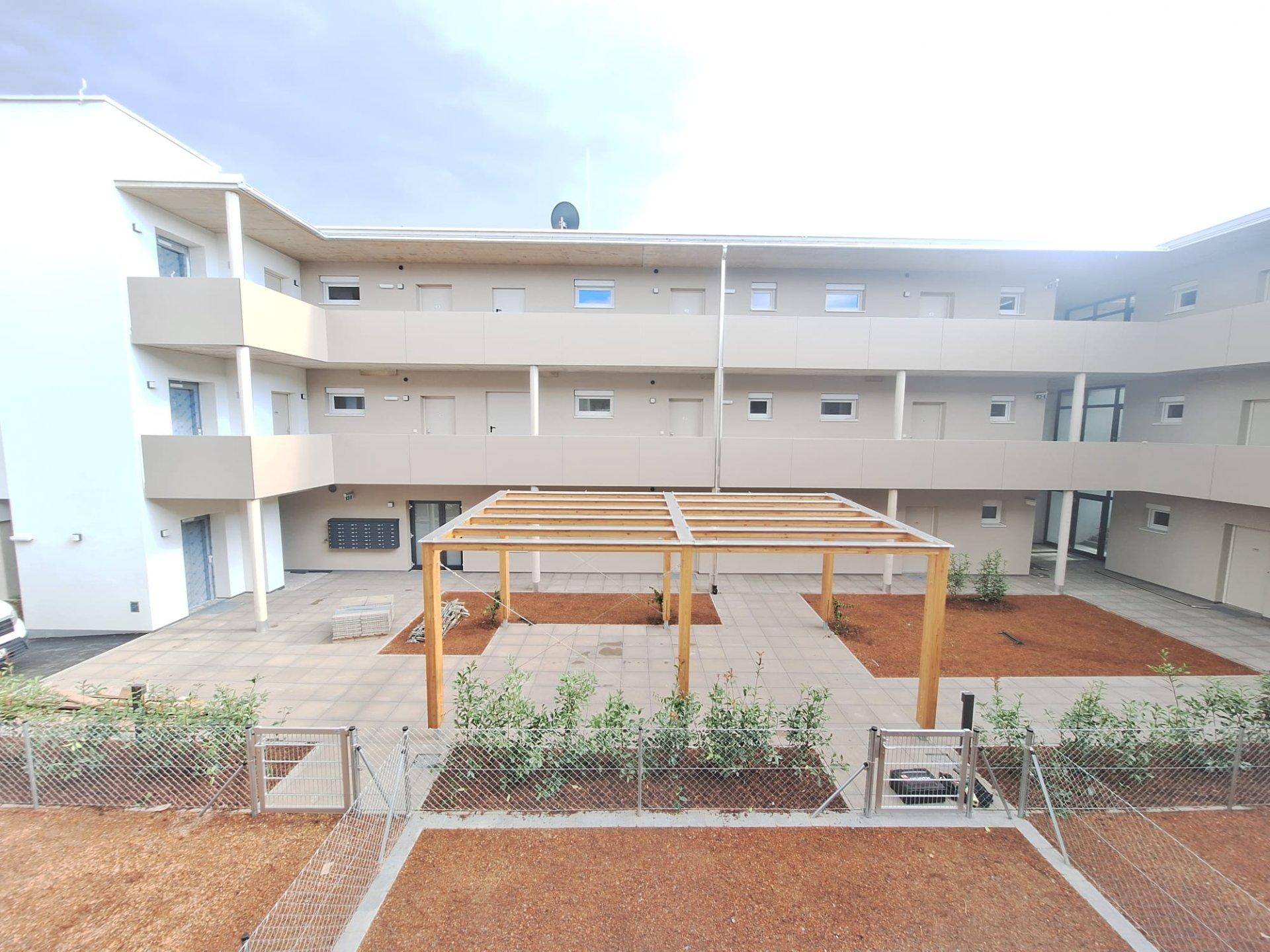 Geräumiger Innenhof eines modernen Wohnkomplexes mit Pergola und neu angelegten Grünflächen.