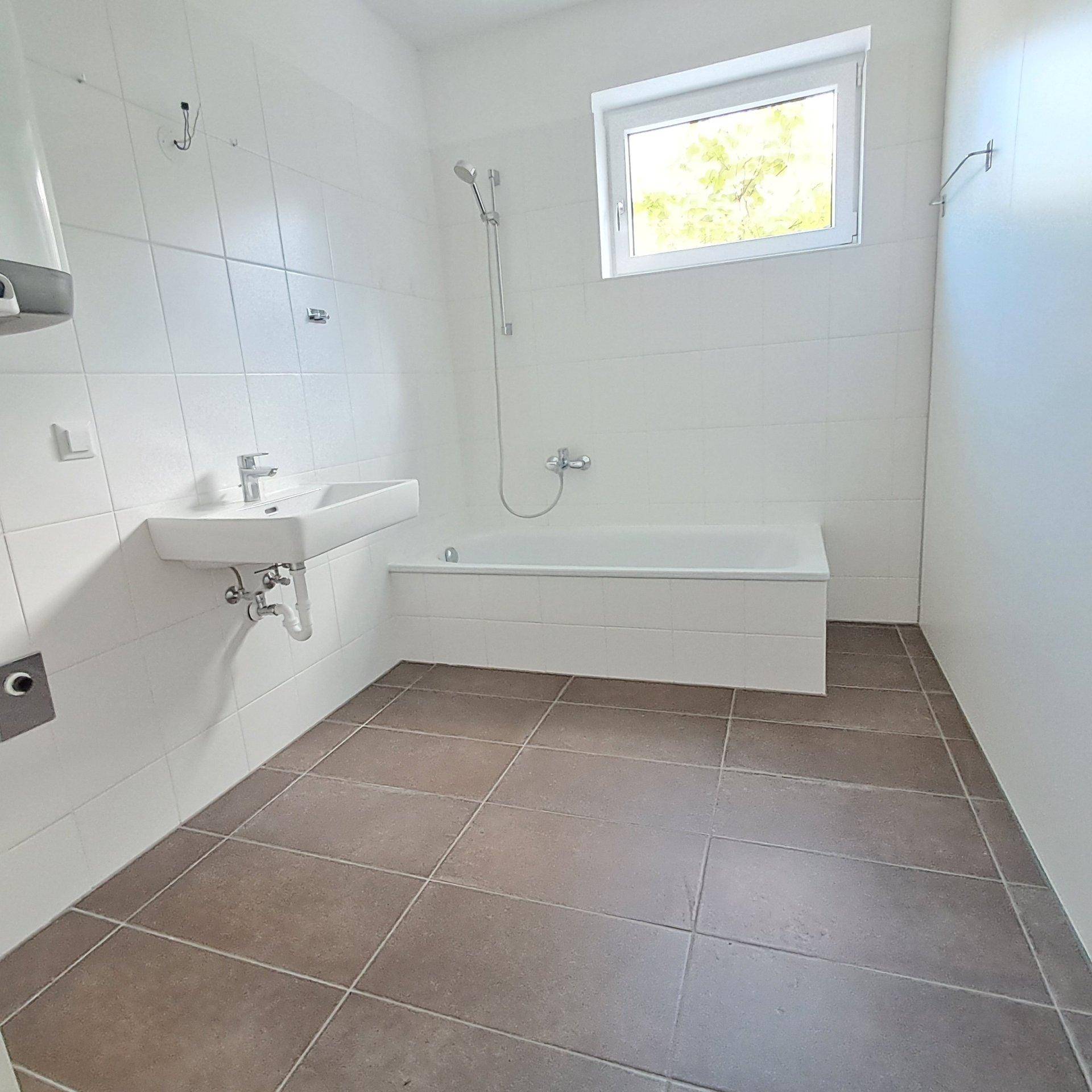 Helles Badezimmer mit Badewanne, Waschbecken und Fenster, komplett gefliest.