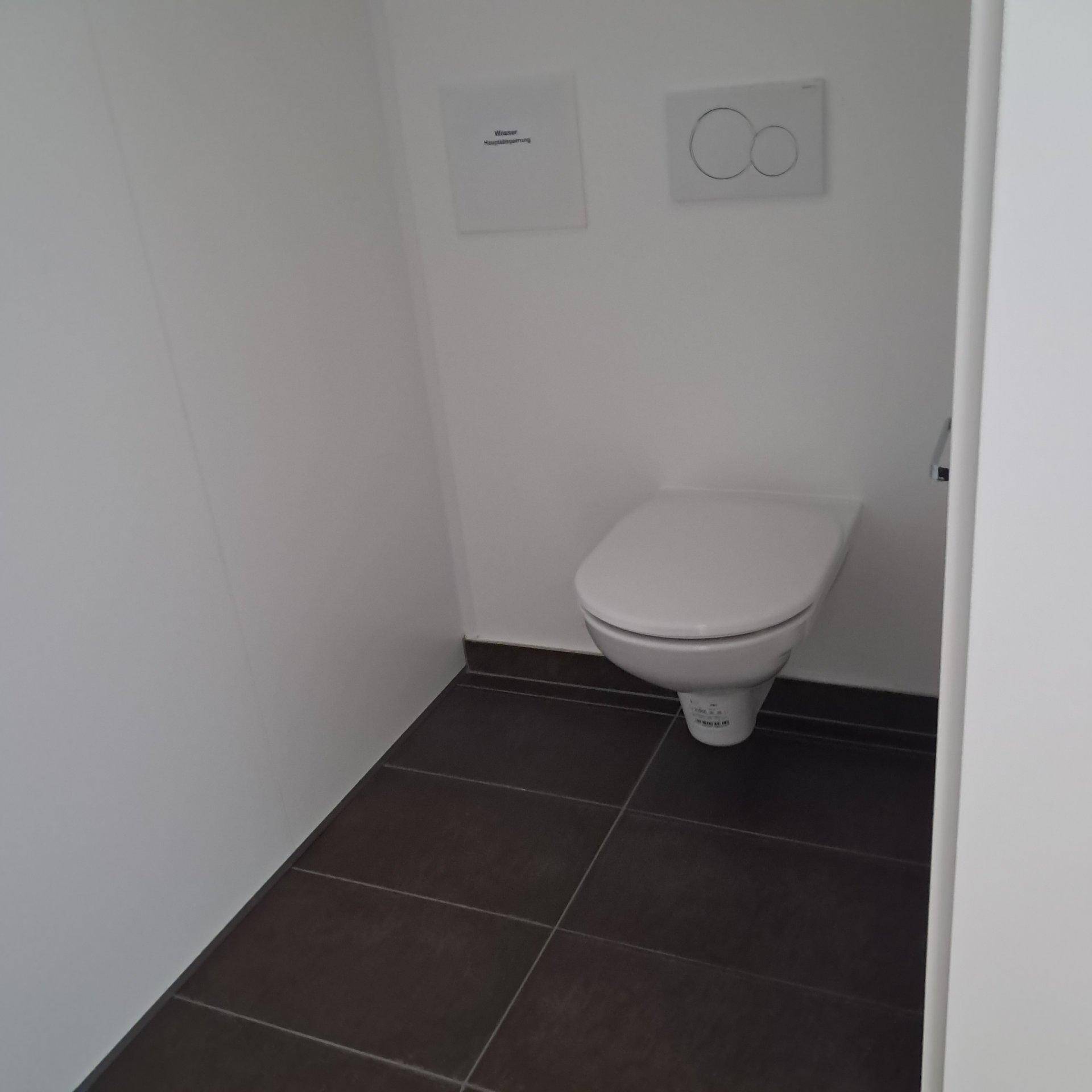 Kleines Gäste-WC mit wandhängender Toilette und dunklen Bodenfliesen.