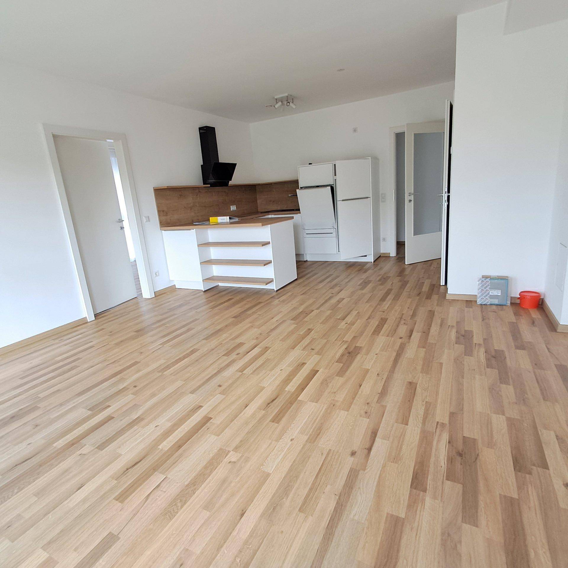 Heller offener Wohnbereich mit Holzboden und integrierter Küche.
