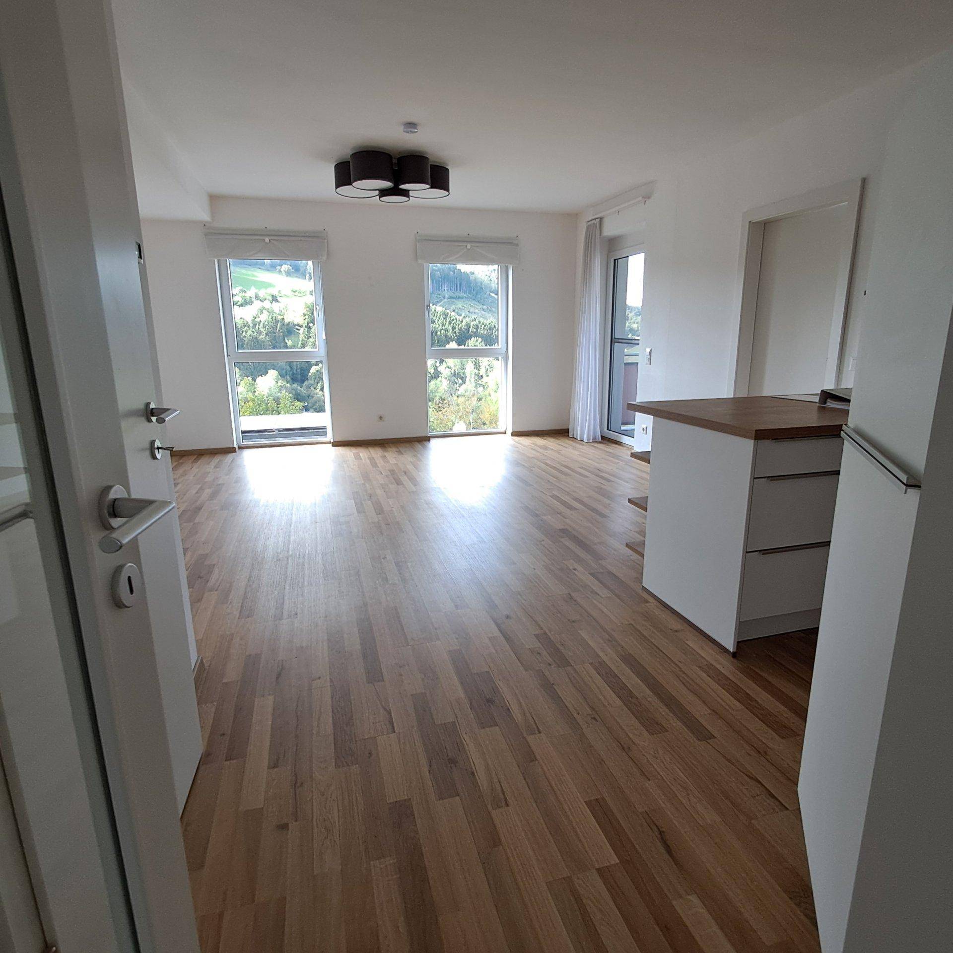 Geräumiger Wohnbereich mit großen Fenstern, Holzboden und Blick ins Grüne.