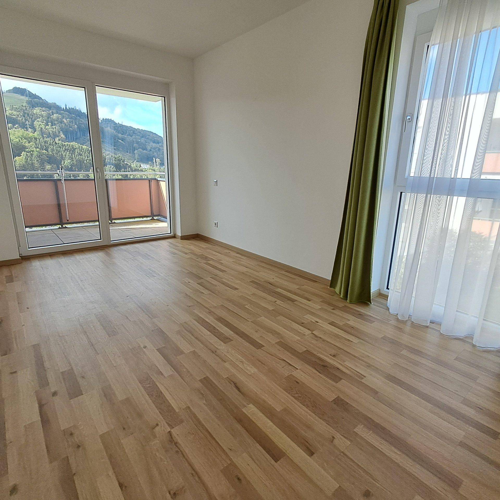 Helles Schlafzimmer mit Holzboden, großen Fenstern und Zugang zum Balkon mit Bergblick.