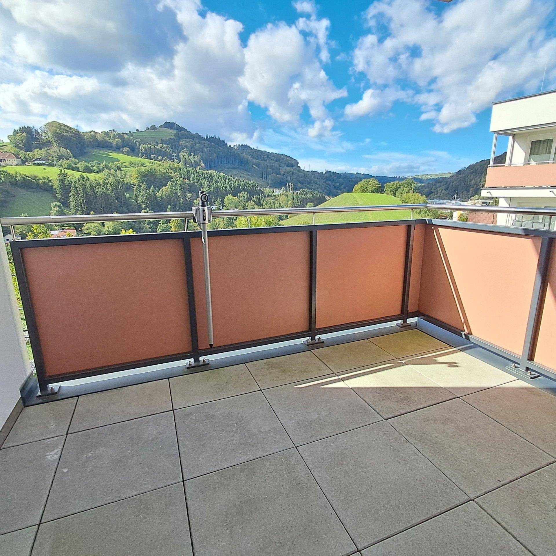 Geräumiger Balkon mit Fliesenboden und weitem Blick auf die umliegende grüne Landschaft.