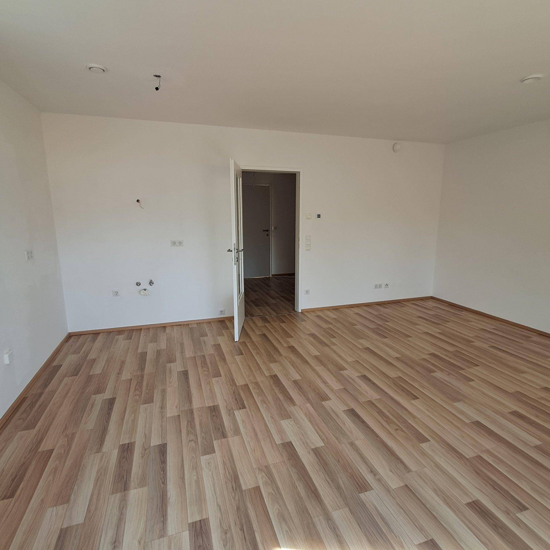 Geräumiger, heller Raum mit Laminatboden und weißen Wänden, ideal für Wohn- oder Schlafzimmer.