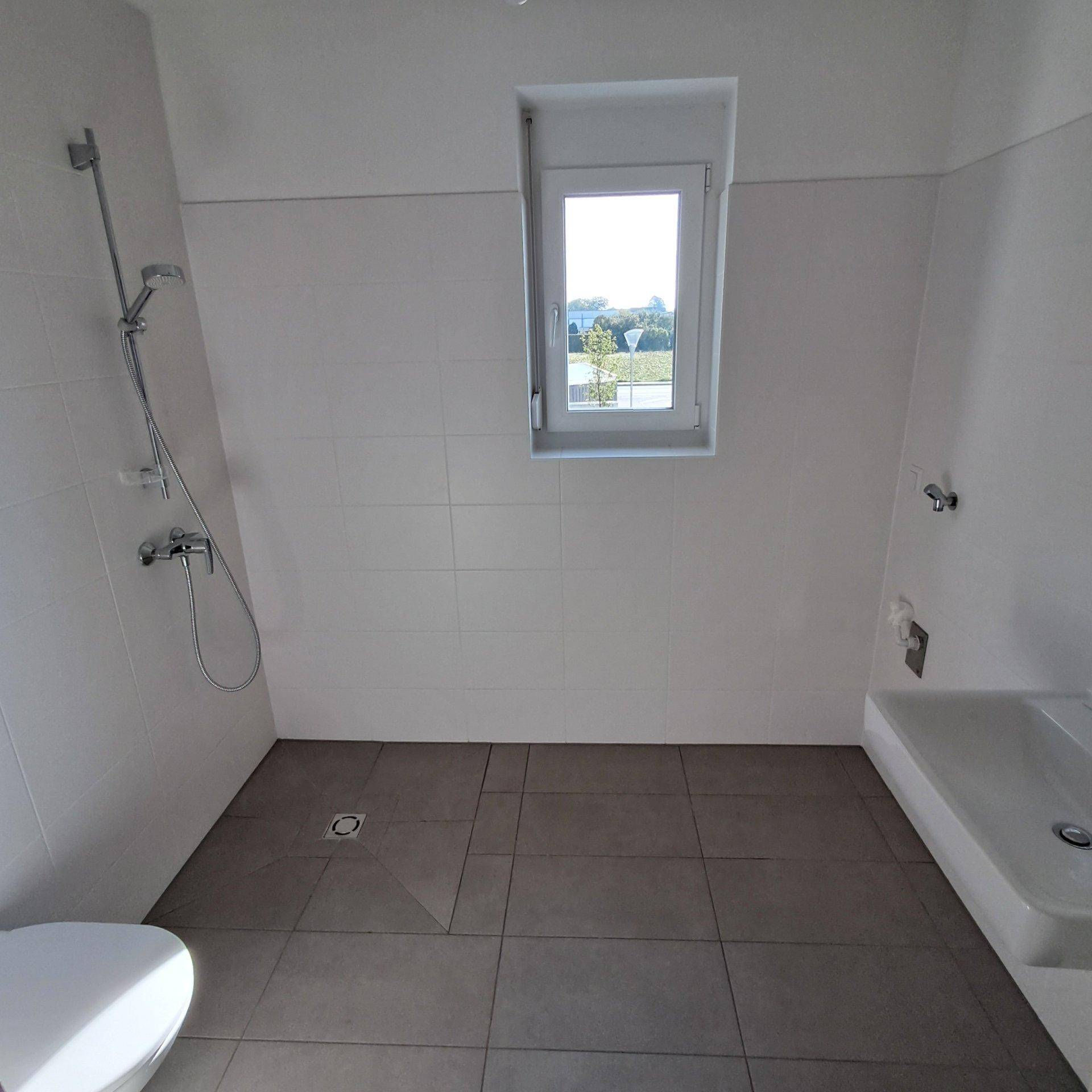 Modernes Badezimmer mit grauen Bodenfliesen, weißer Wandverkleidung und Fenster für Tageslicht.