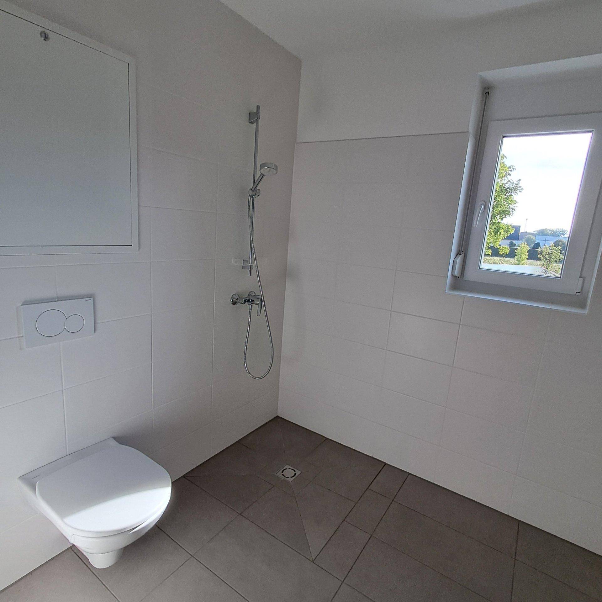 Funktionales Badezimmer mit Duschbereich, wandhängendem WC und Fenster für gute Belüftung.