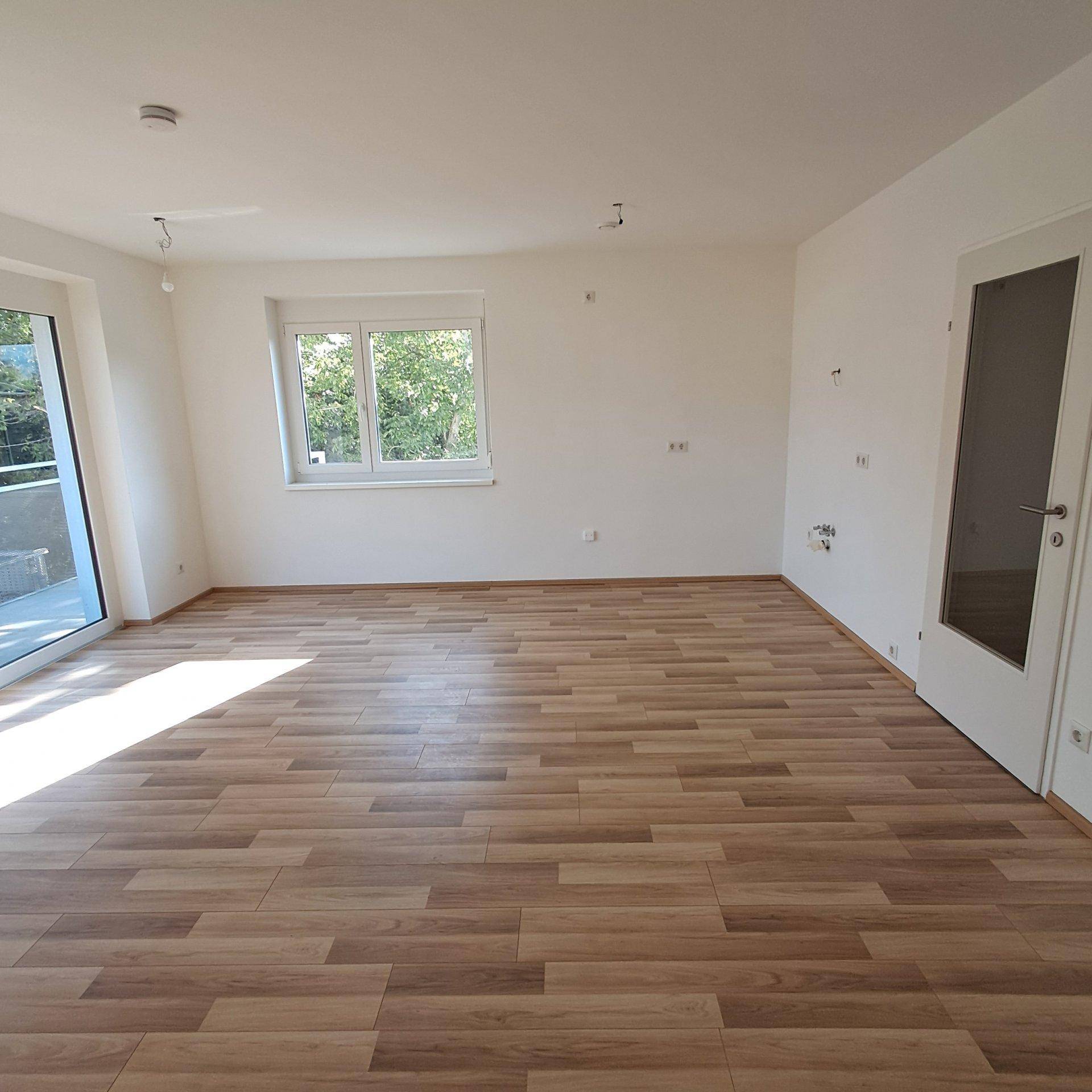 Geräumiger, heller Wohnbereich mit Laminatboden und direktem Zugang zum Balkon.