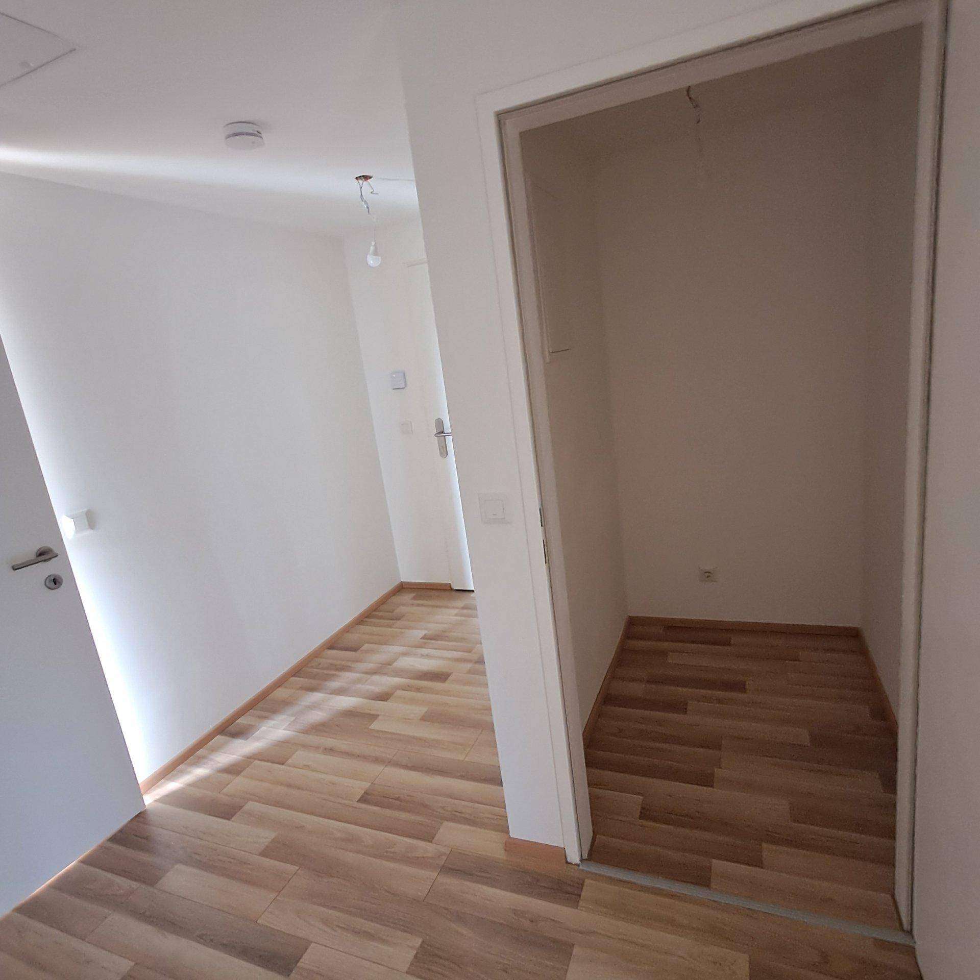 Heller Flur mit Laminatboden und Zugang zu einem praktischen Abstellraum.