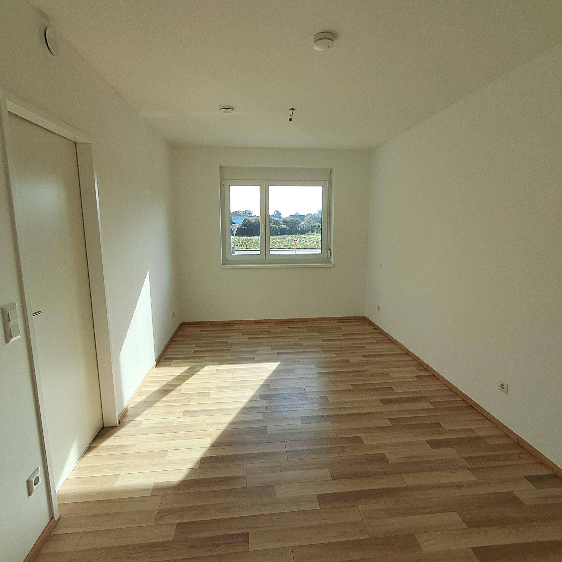 Sonniger Raum mit Laminatboden und weiß gestrichenen Wänden, ideal als Schlafzimmer.