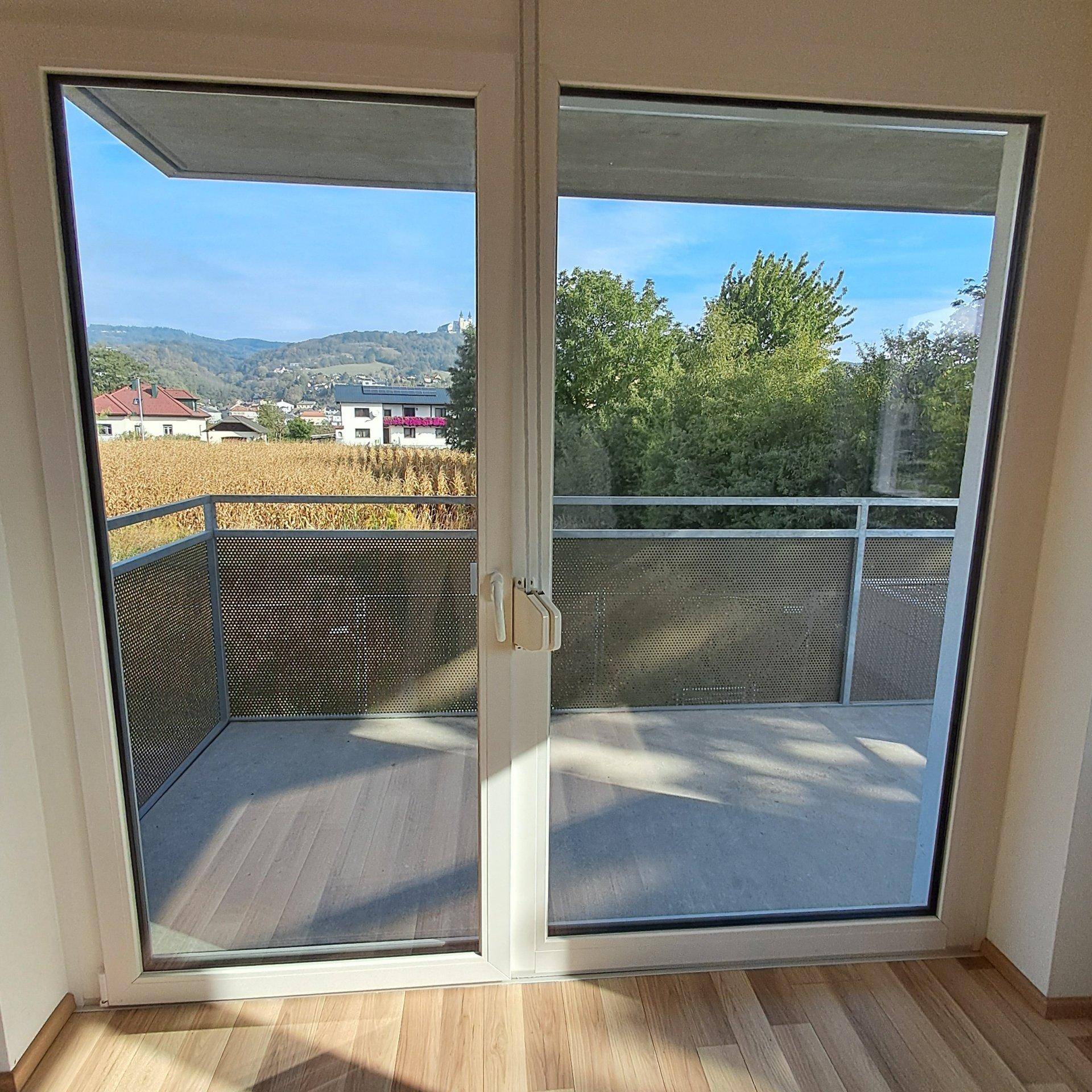 Heller Innenraum mit großem Glasfenster und Balkonzugang, bietet weite Aussicht.