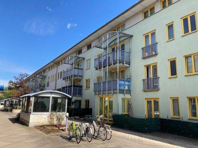 Lange Fassade eines modernen Wohngebäudes mit Balkonen und Fahrradstellplätzen im Freien.
