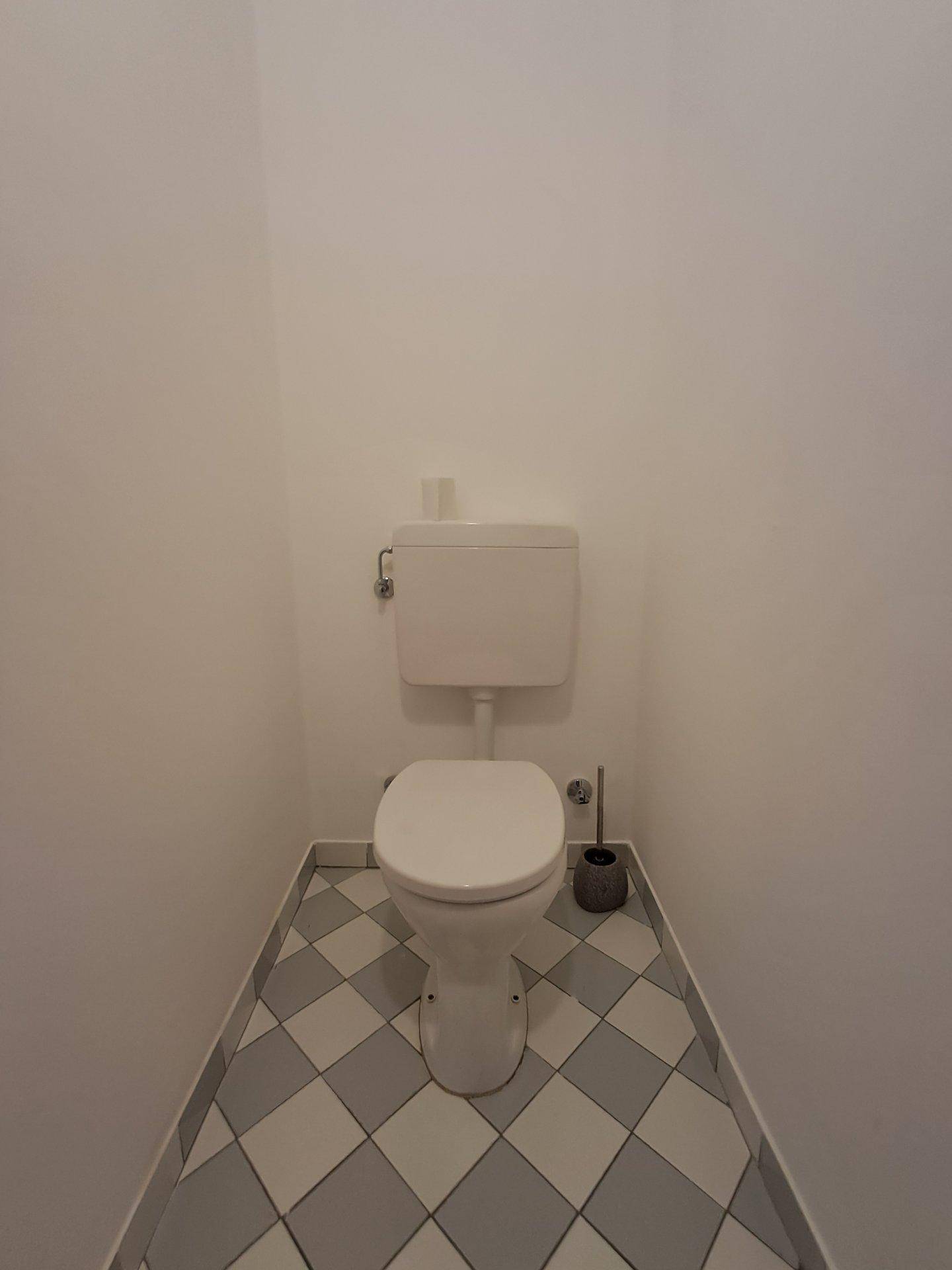 Kleines, separates WC mit Stand-WC und grau-weiß kariertem Fliesenboden.