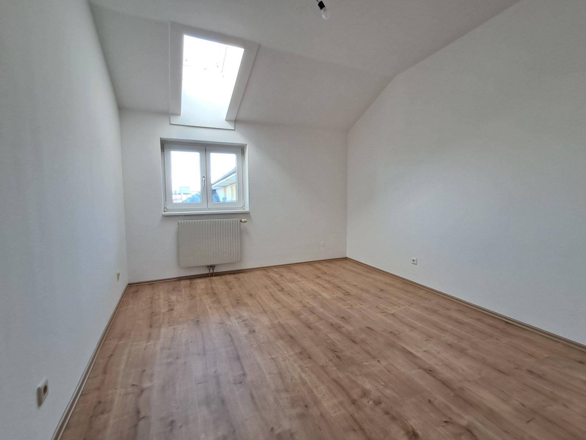 Geräumiges, helles Zimmer mit Laminatboden, Dachfenster und Blick ins Grüne.