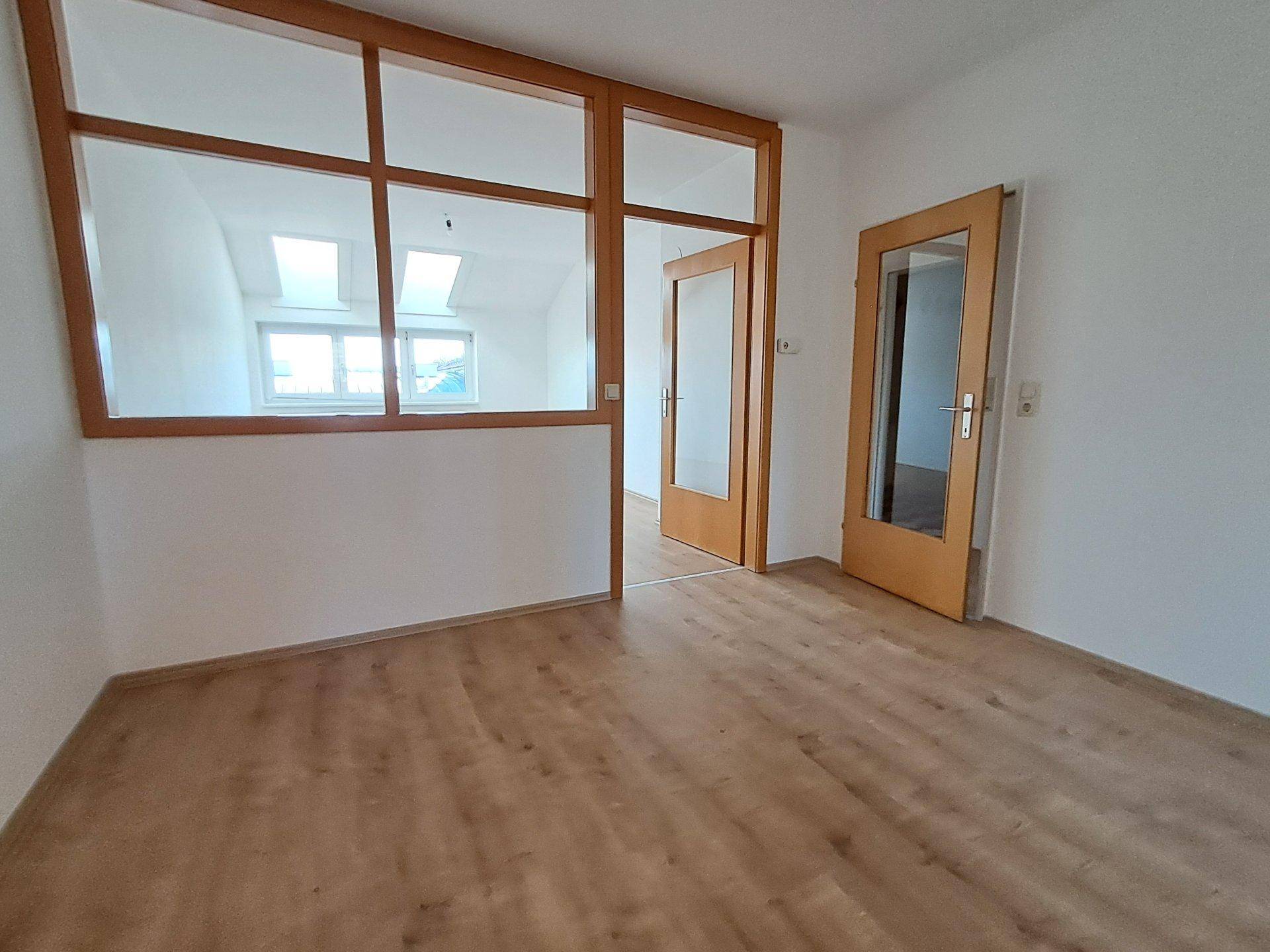 Leerer Raum mit Laminatboden und einer Holztrennwand mit Glaselementen, vielseitig nutzbar.