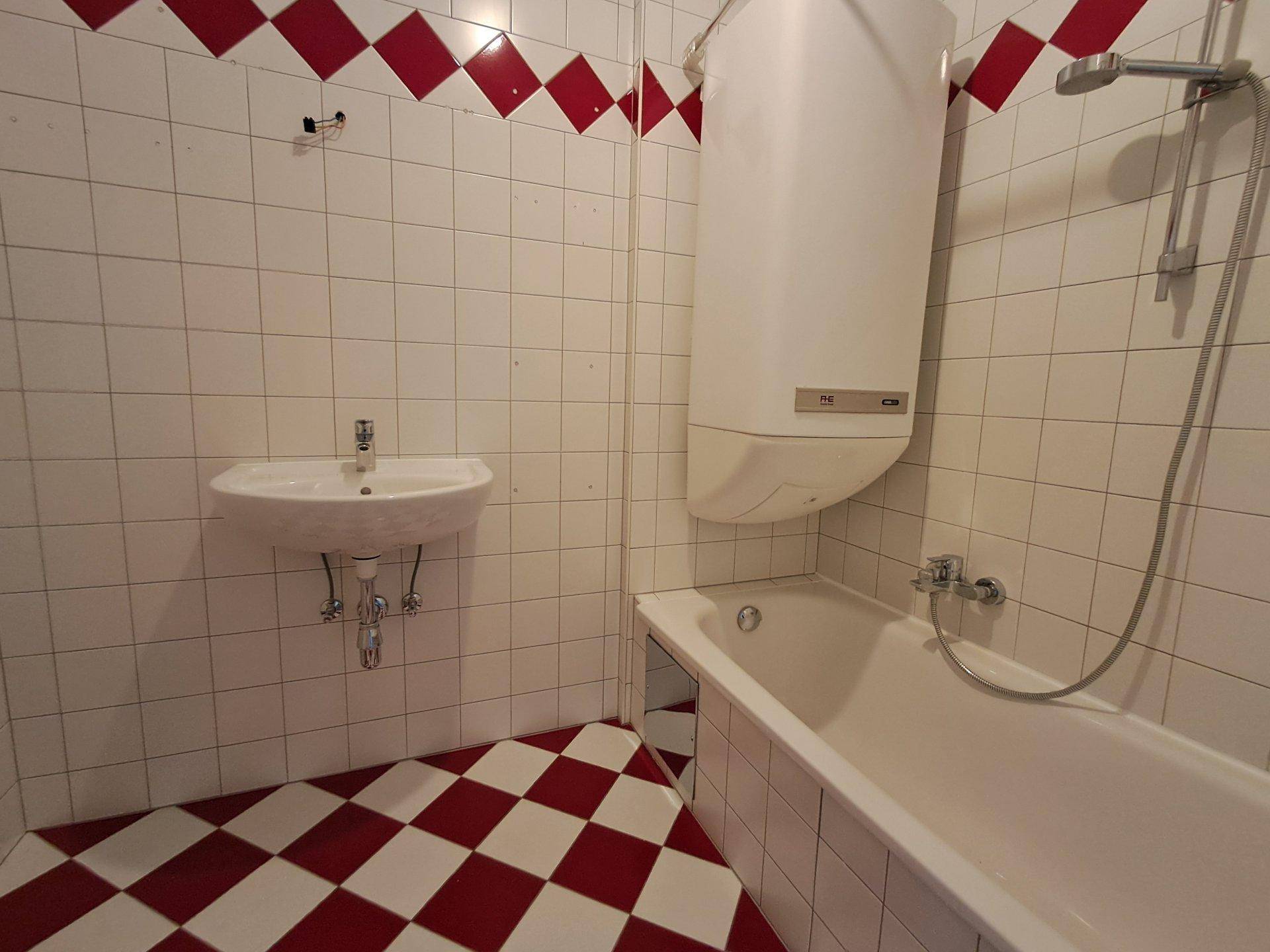 Badezimmer mit Badewanne, Waschbecken und auffälligen rot-weiß karierten Fliesen.