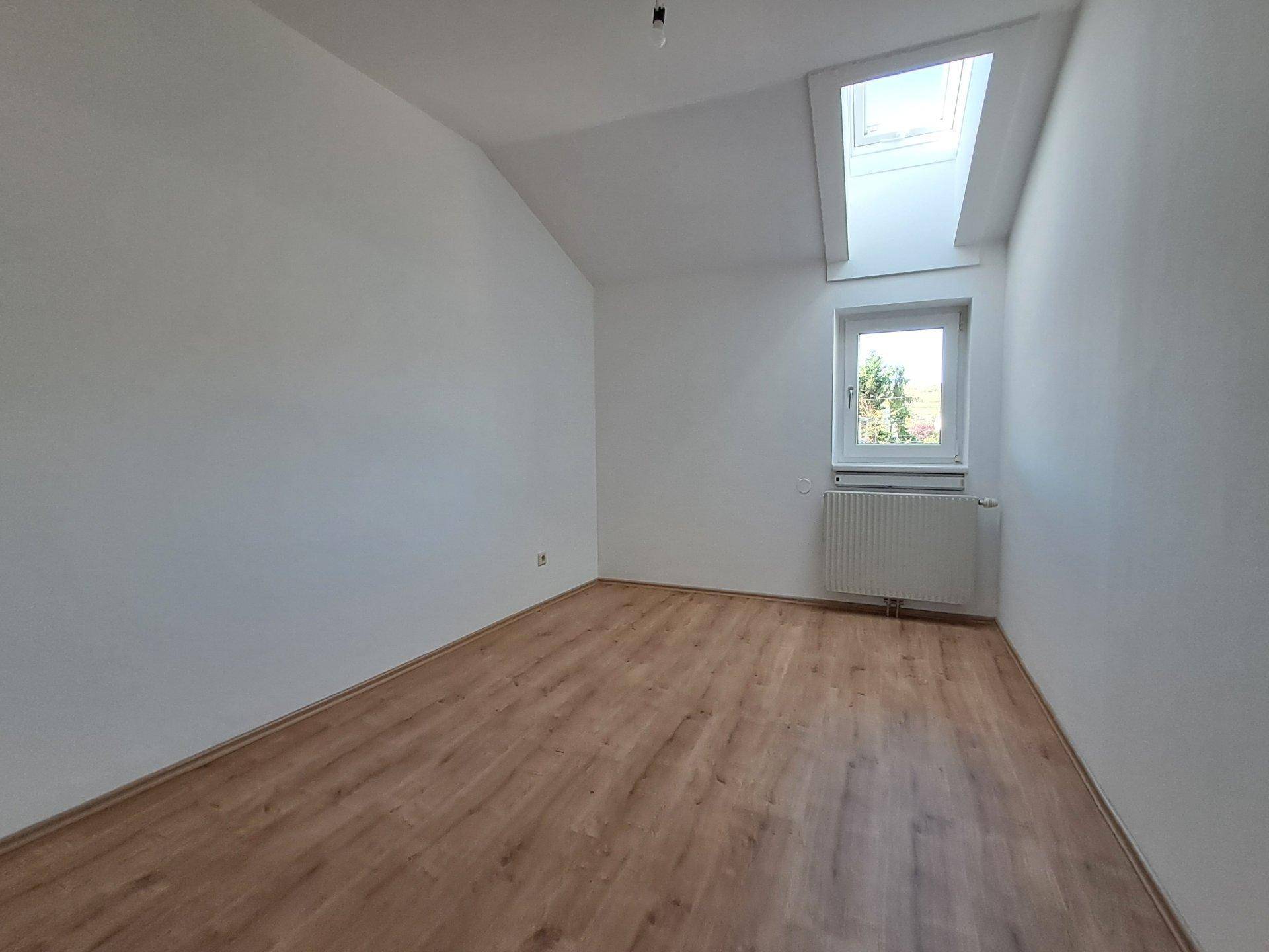Helles, leeres Zimmer mit Laminatboden, Dachfenster und Heizkörper, ideal als Schlafzimmer.