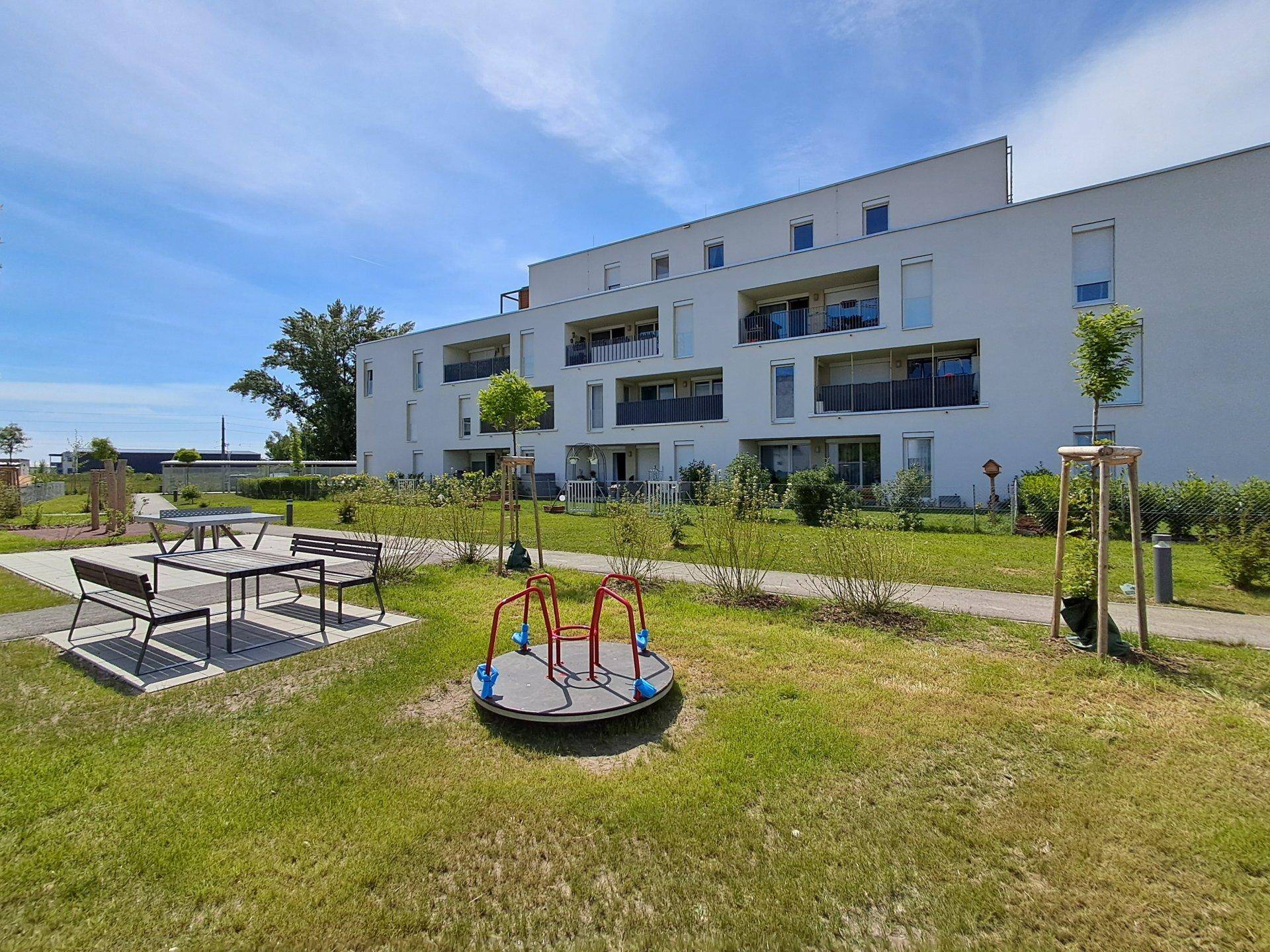 Moderne Wohnanlage mit Spielplatz, Sitzgelegenheiten und gepflegten Grünflächen im Freien.