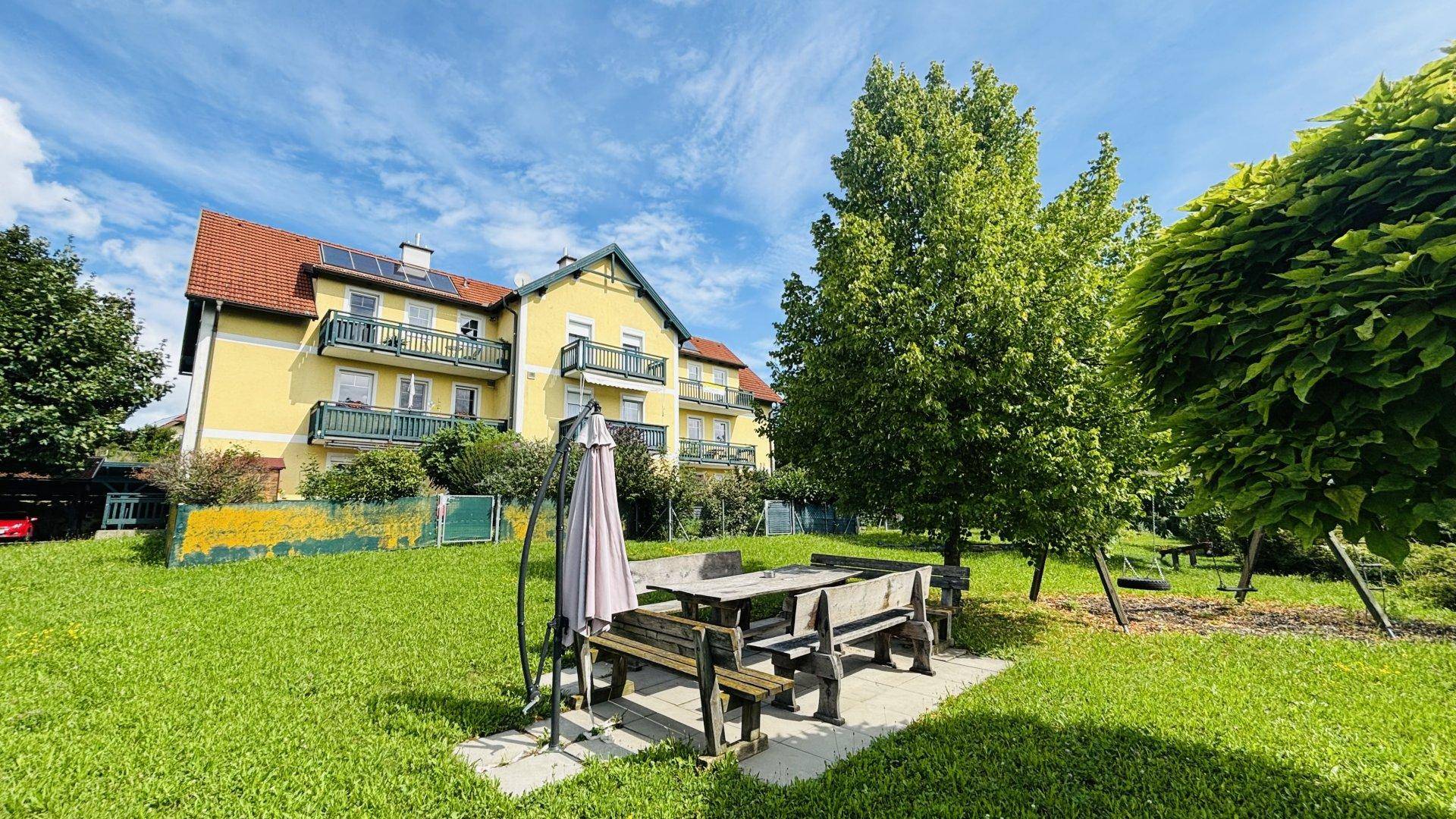 Große grüne Rasenfläche mit rustikalem Holztisch und Bänken, ideal für Mahlzeiten im Freien.
